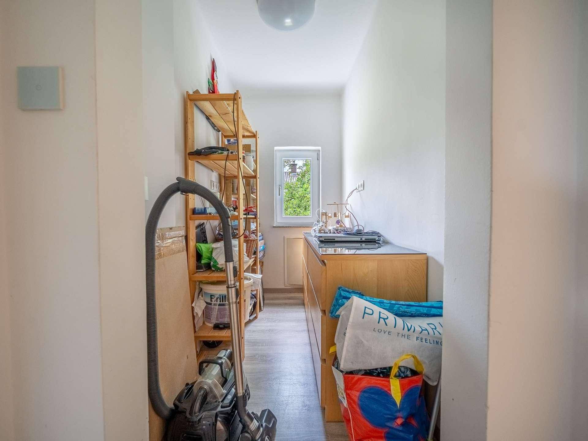 Schmaler Abstellraum mit Fenster, Regalen und Haushaltsgeräten.