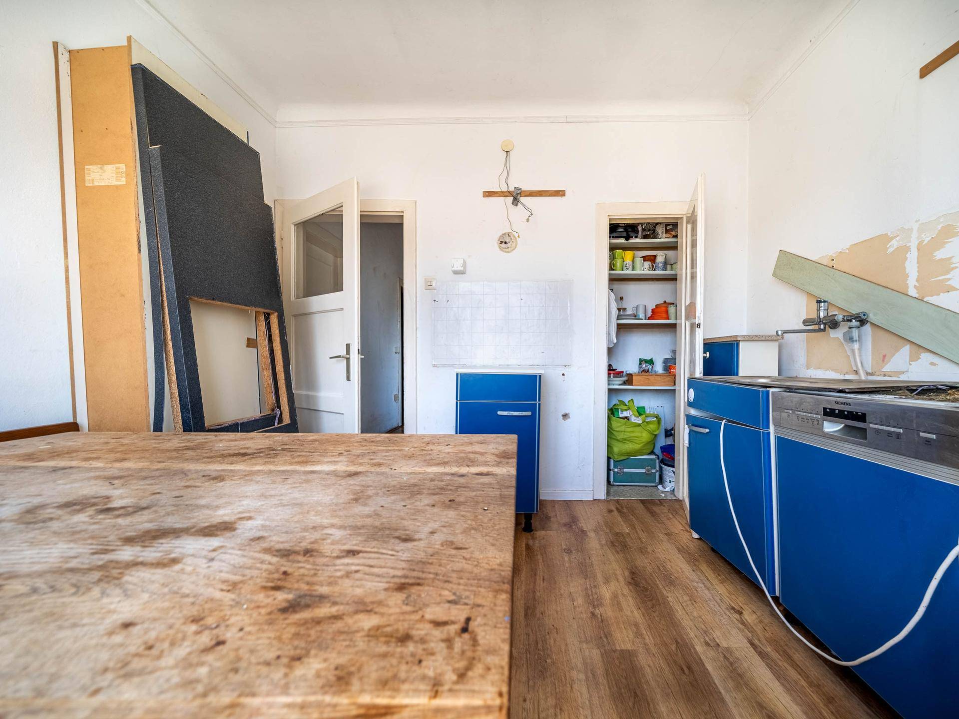 Renovierungsbedürftige Küche mit blauen Schränken, Spüle und offenem Regal.