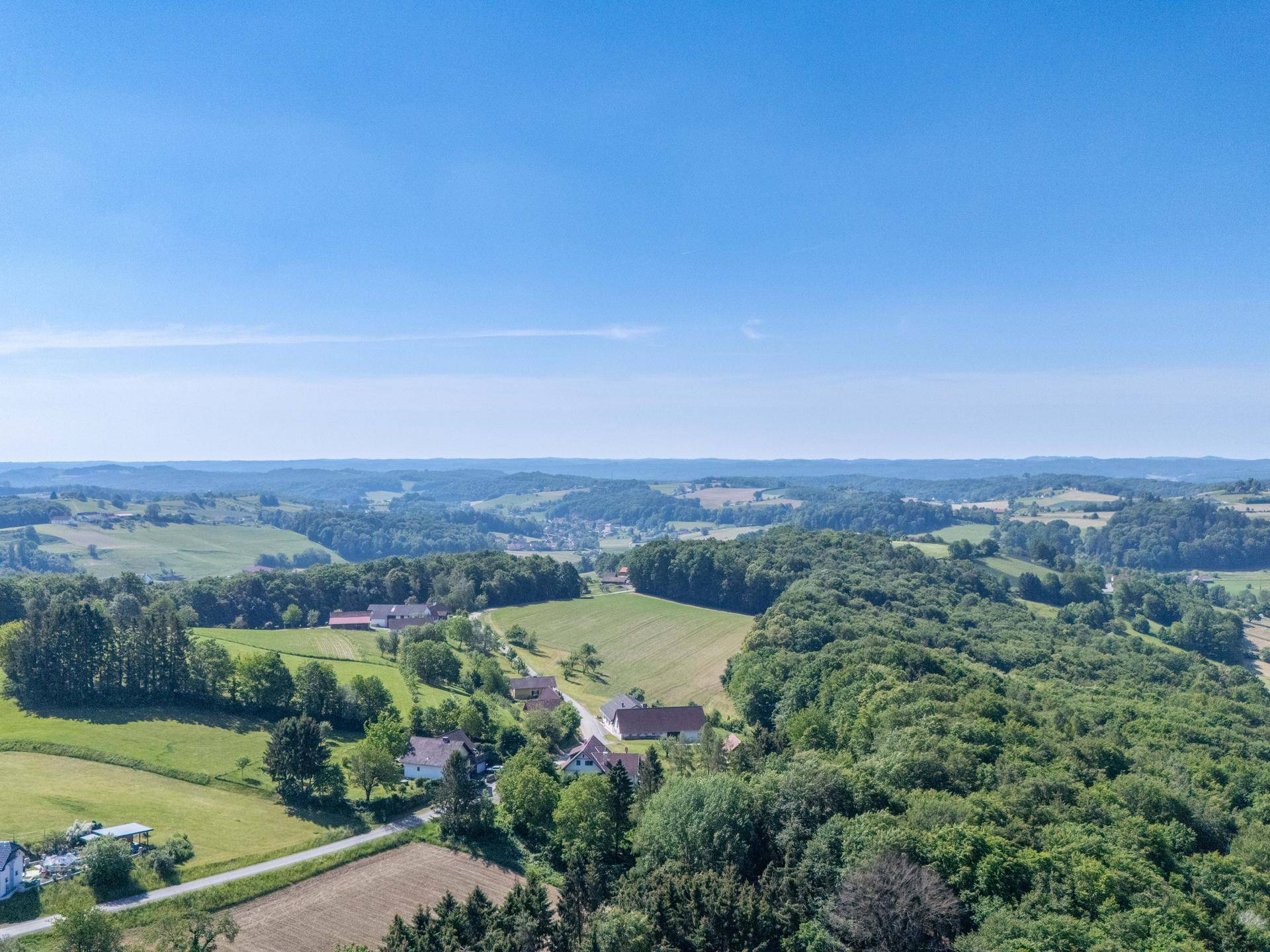 Weitläufige Luftaufnahme der malerischen Landschaft mit Wäldern, Feldern und verstreuten Häusern.
