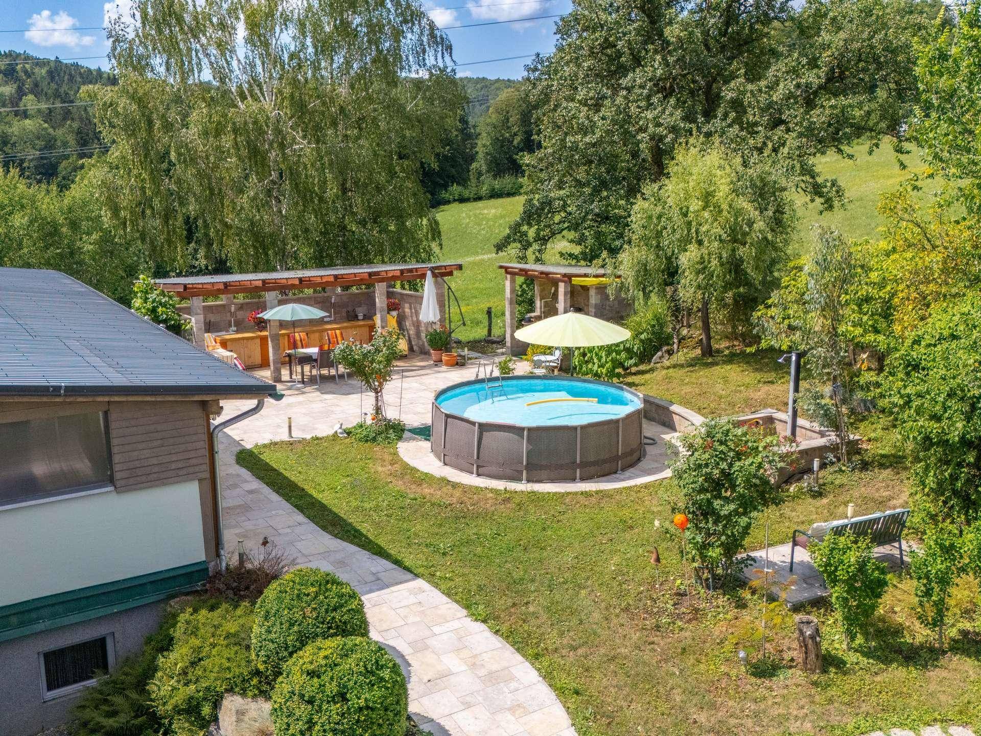 Gartenbereich mit Aufstellpool, gepflasterter Terrasse, Essbereich und überdachter Außenküche.