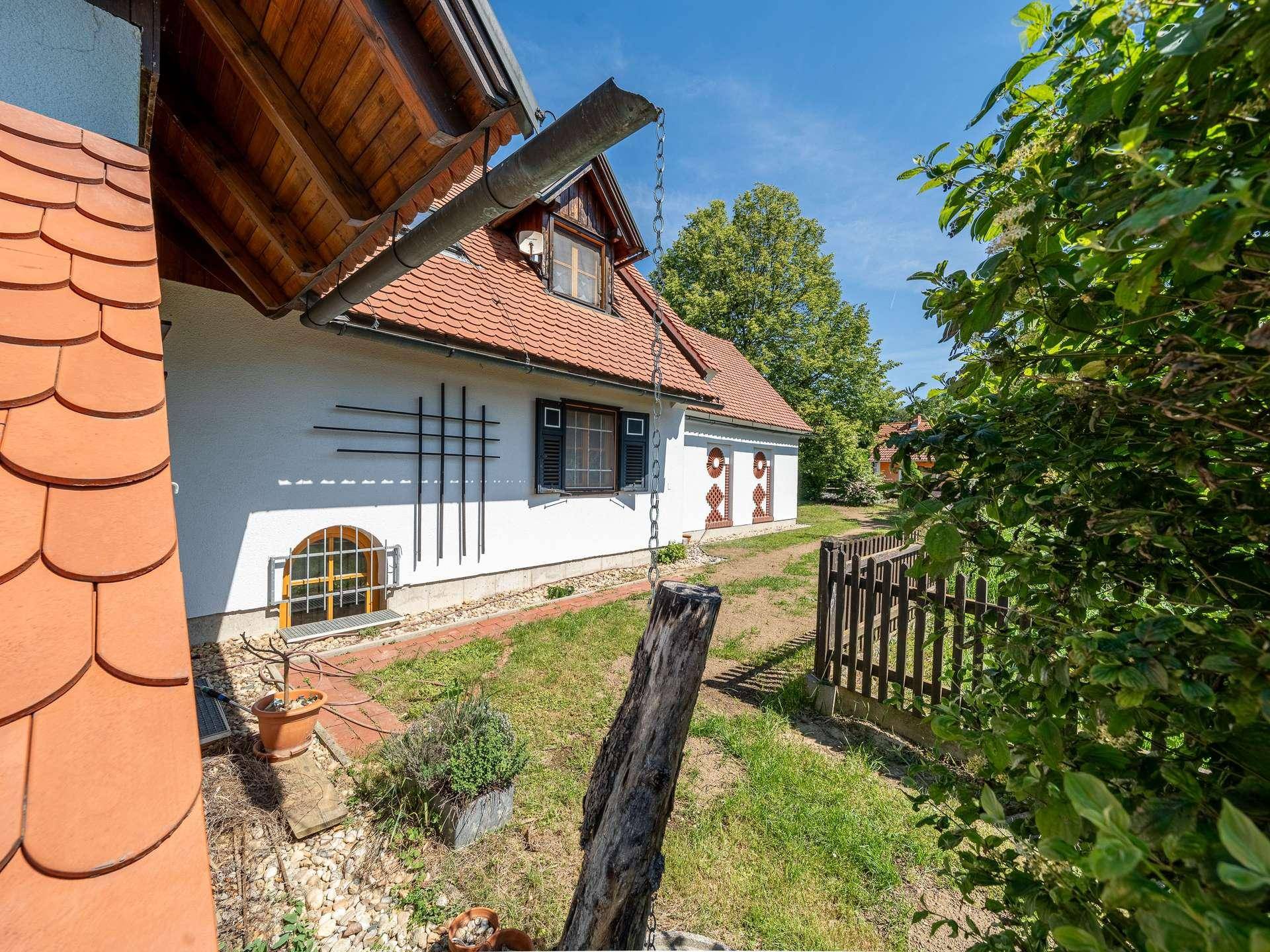 Seitenansicht des Hauses mit kleinem Gartenbereich, Holzzaun und Dachüberstand.