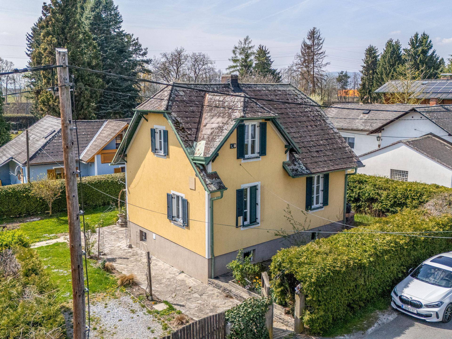 Seitenansicht des Hauses aus der Vogelperspektive mit Garten, Hecken und angrenzender Straße.