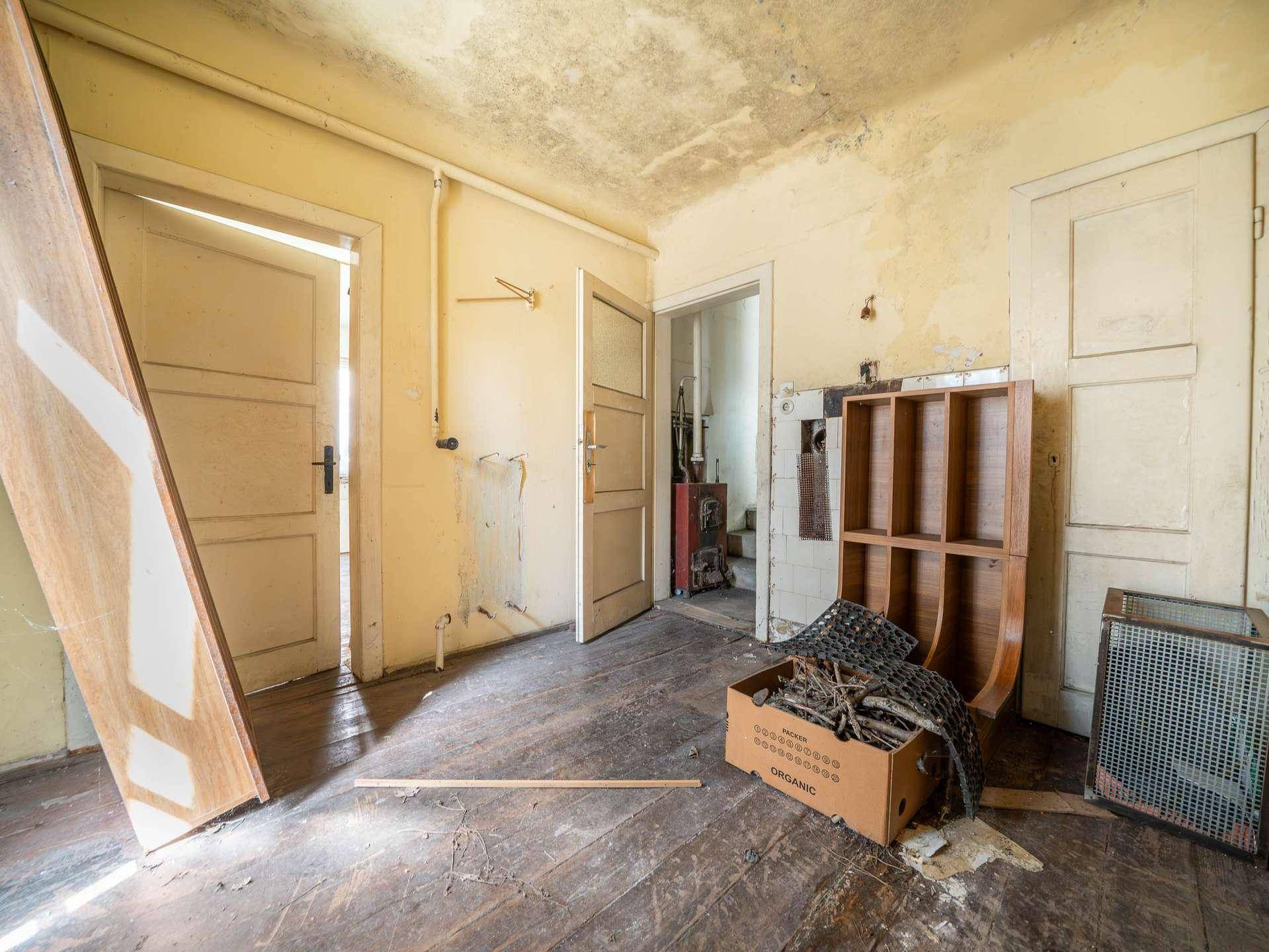Unfertiger Raum mit Holzboden und mehreren Türen, der auf eine Renovierung wartet.