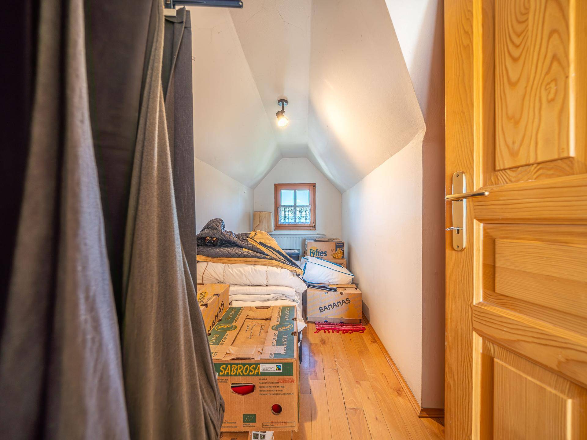 Dachbodenbereich mit Holzfußboden, Stauraum und kleinem Fenster unter der Dachschräge.