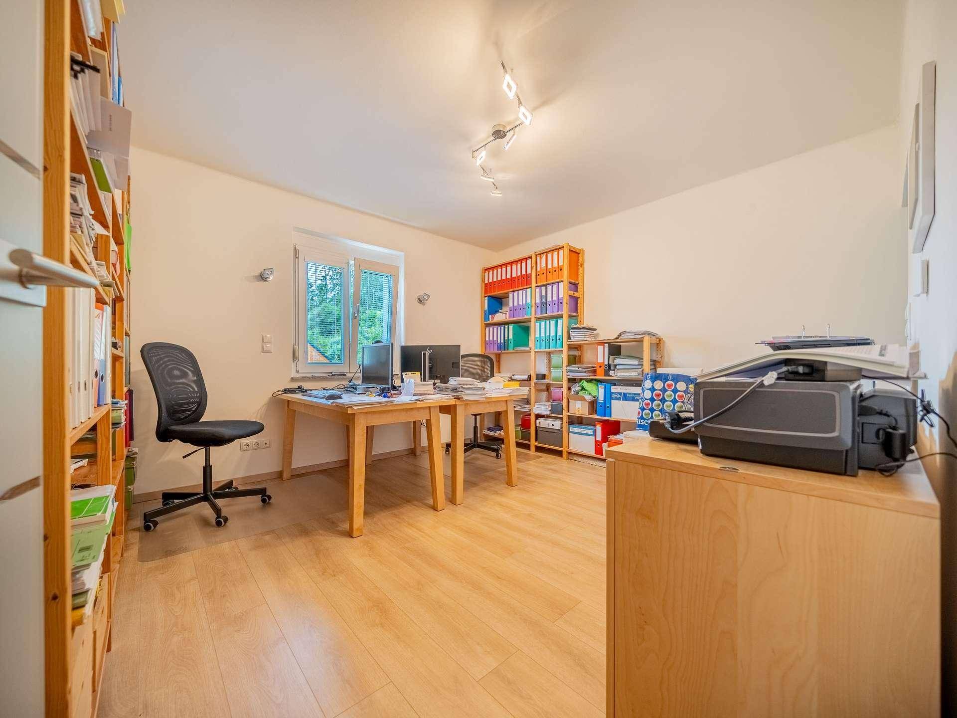 Helles Büro mit zwei Schreibtischen, Regalen und Fenster.