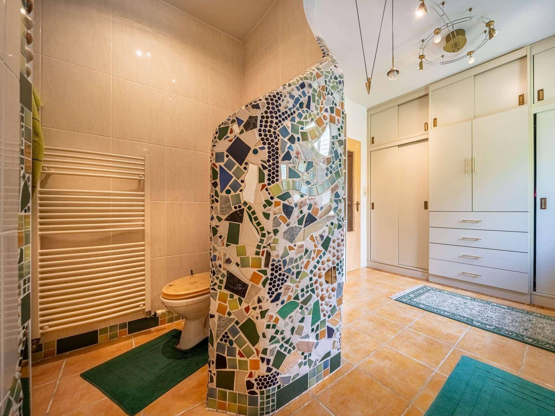 Badezimmer mit WC, Heizkörper und integrierten Schränken, verziert mit Mosaik.