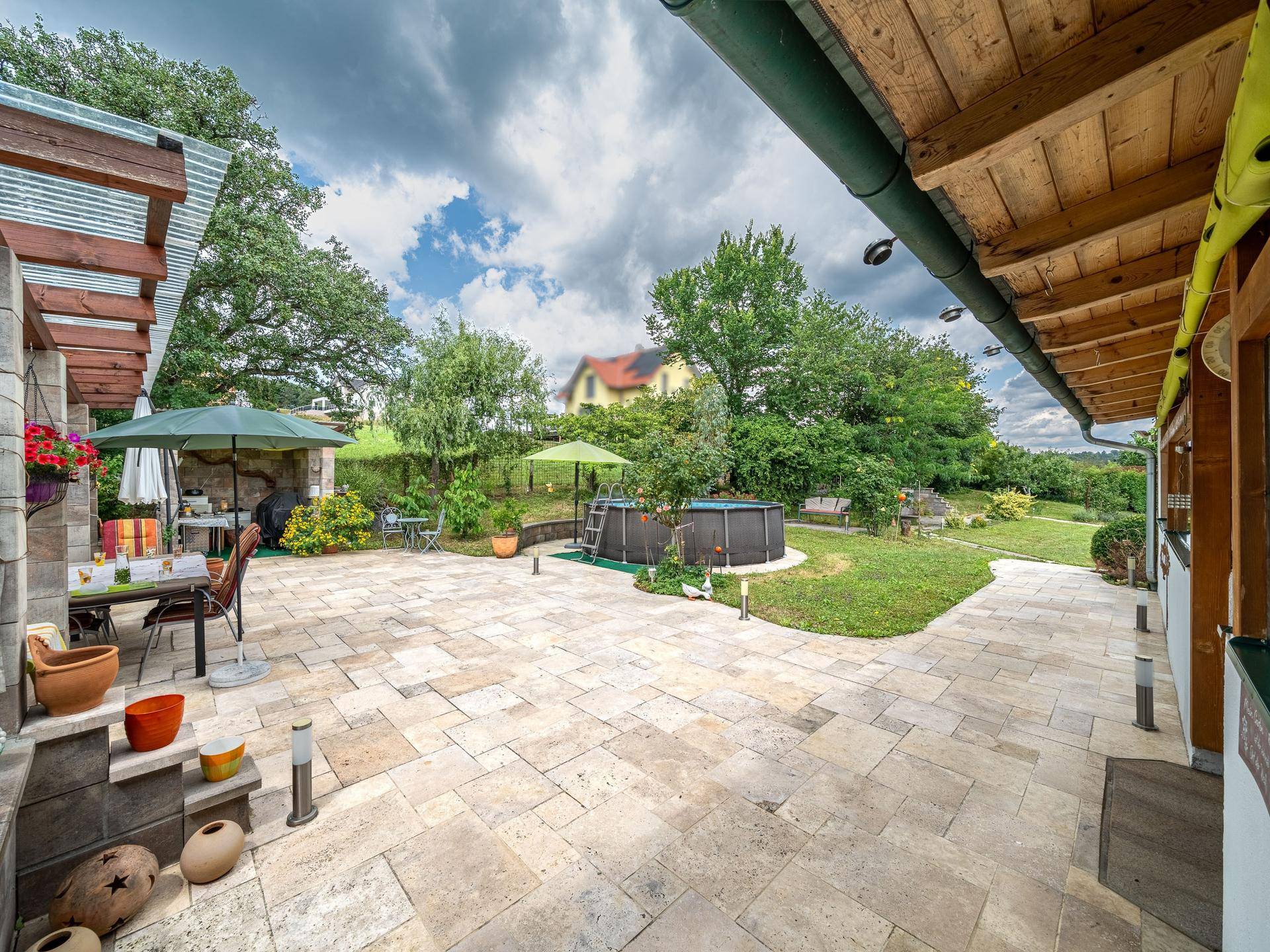 Weitläufige Terrasse mit Zugang zum Garten und einem Aufstellpool, umgeben von viel Grün.