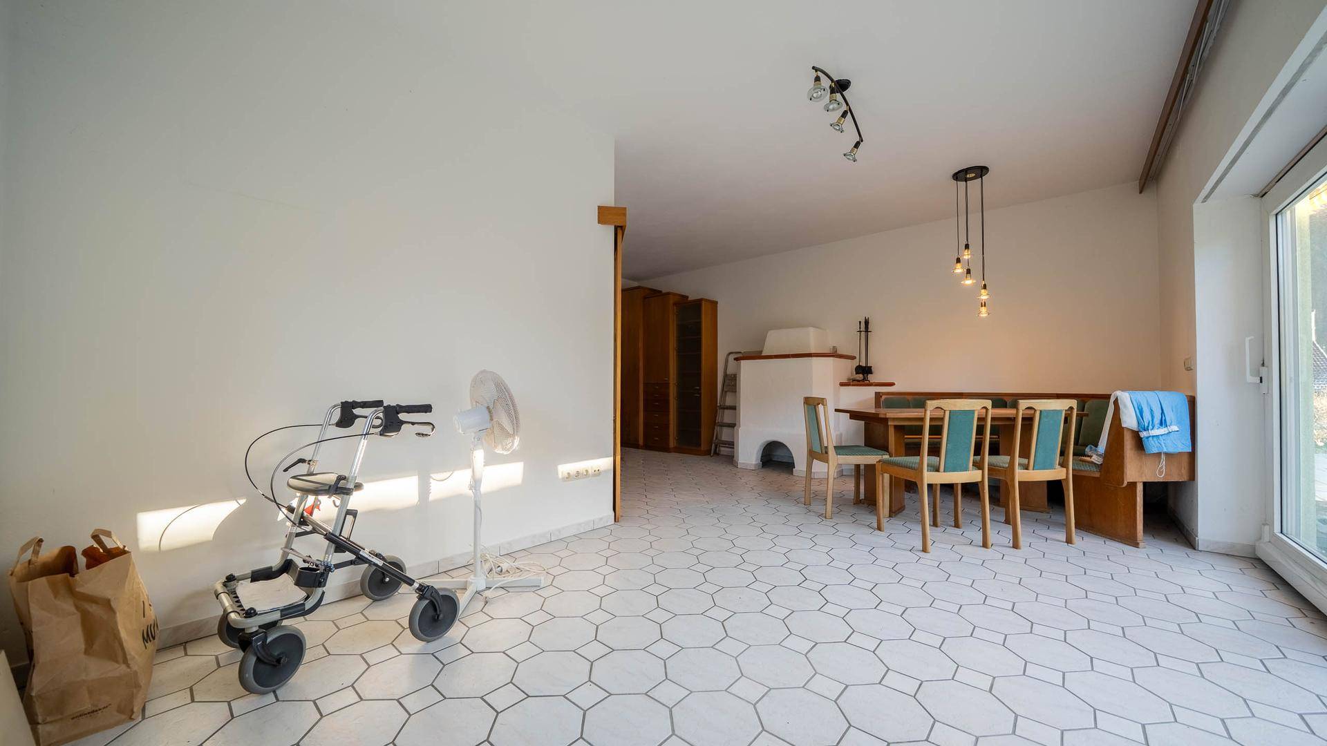 Geräumiger Wohn-Essbereich mit Fliesenboden, Kachelofen und Zugang zur Terrasse.