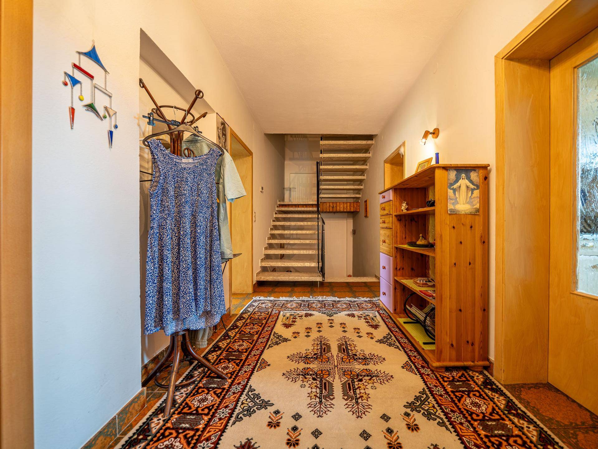 Heller Flur mit Teppichläufer, Holzmöbeln und Treppenaufgang in die obere Etage.
