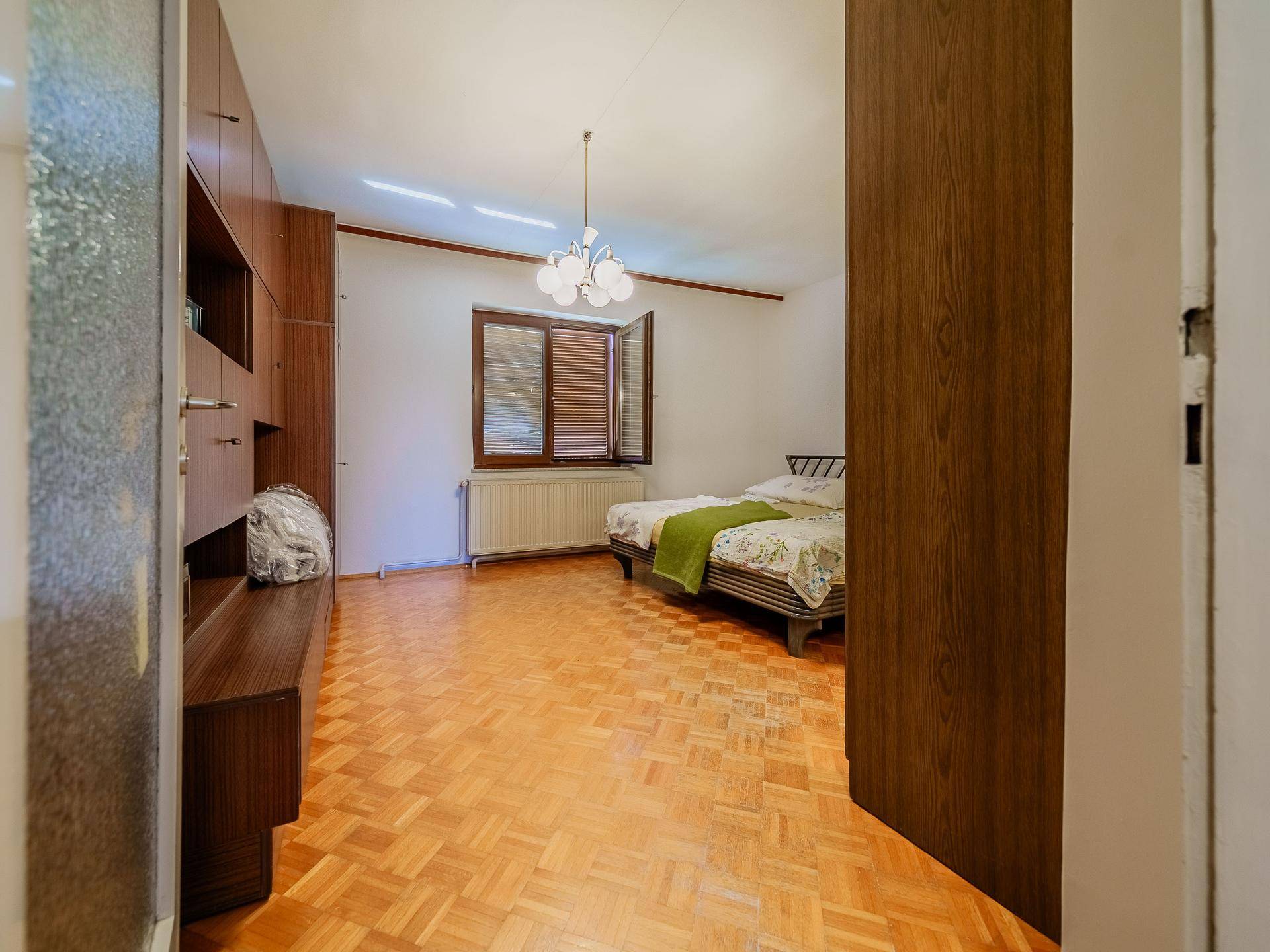 Schlafzimmer mit Parkettboden, Einbauschrank und einem Bett mit Fensterblick.