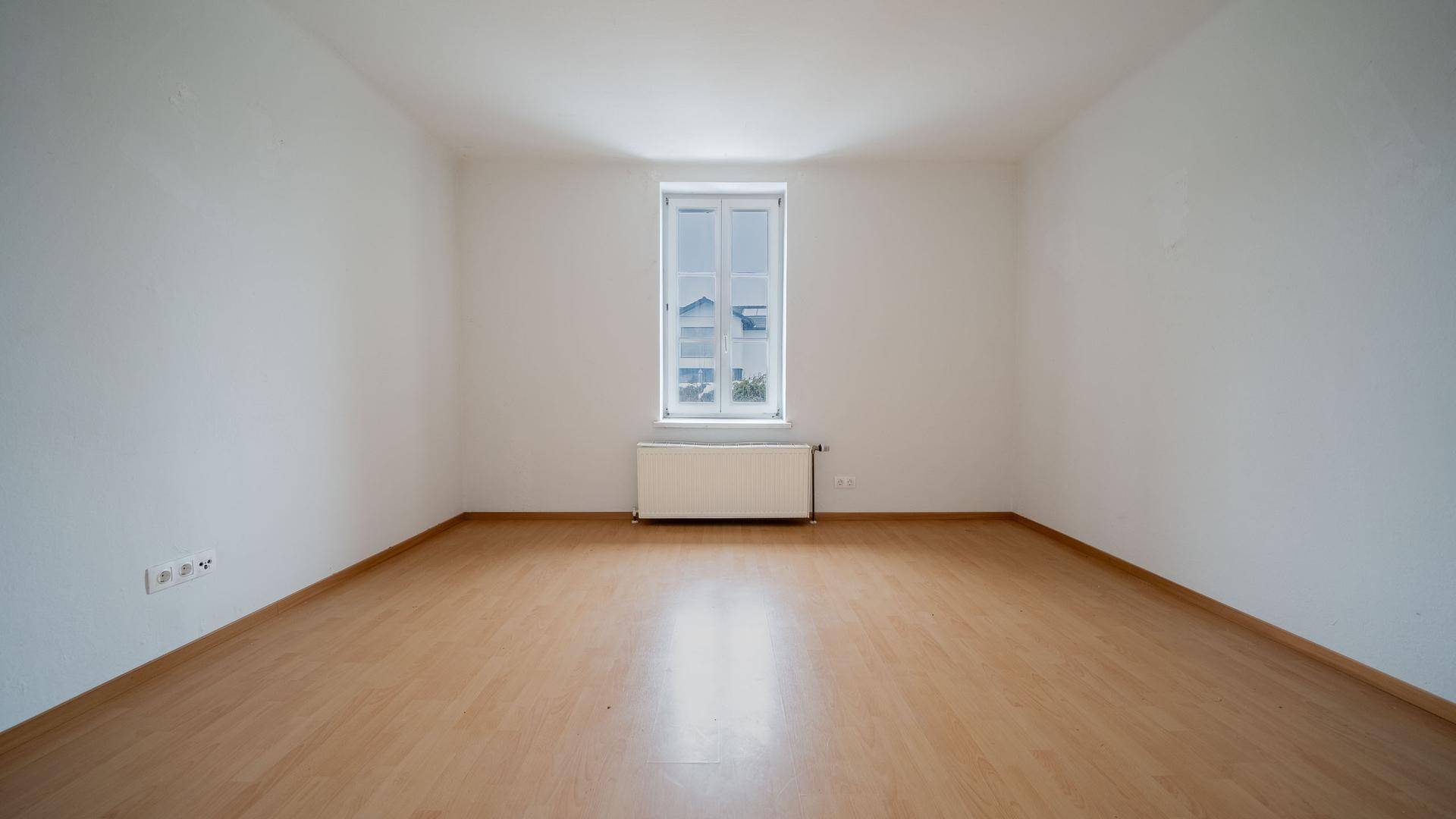 Helles Schlafzimmer mit Holzboden und einem großen Fenster, das viel Tageslicht hereinlässt.