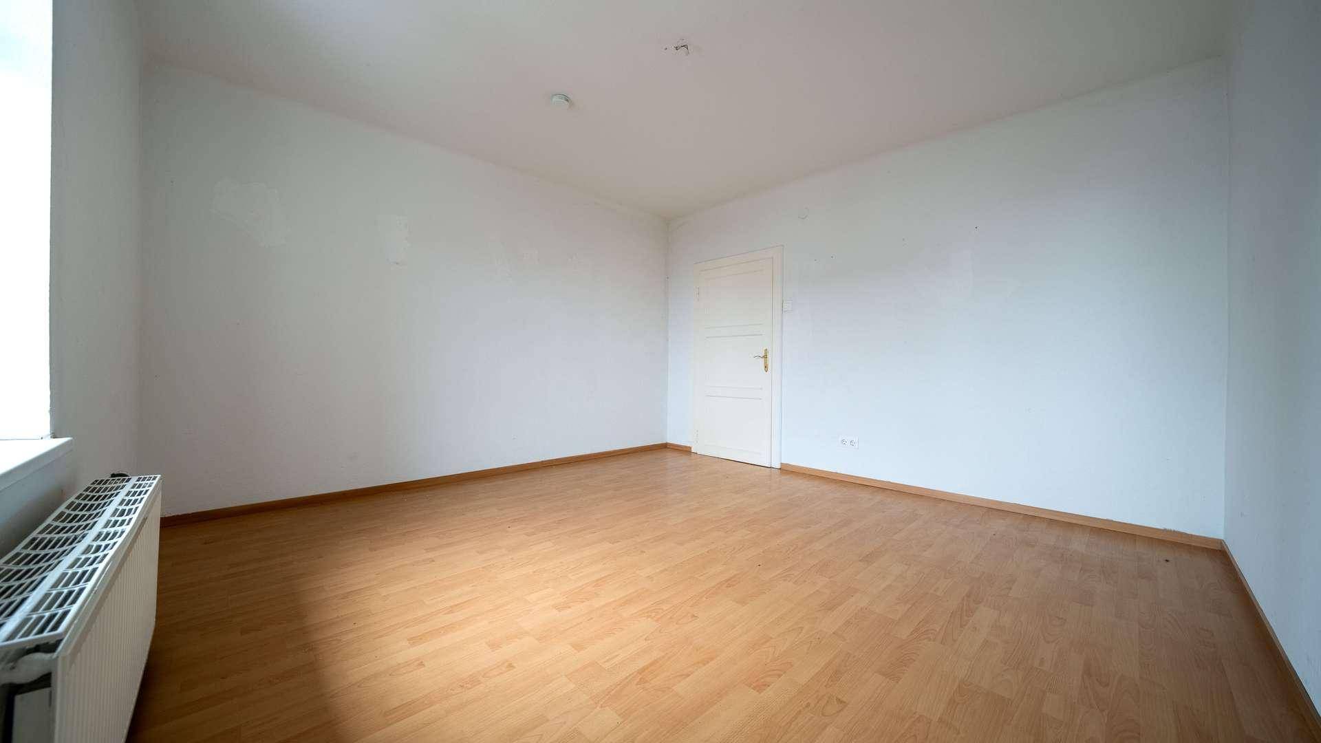 Helles Schlafzimmer mit Laminatboden, weiß gestrichenen Wänden und einer Tür.