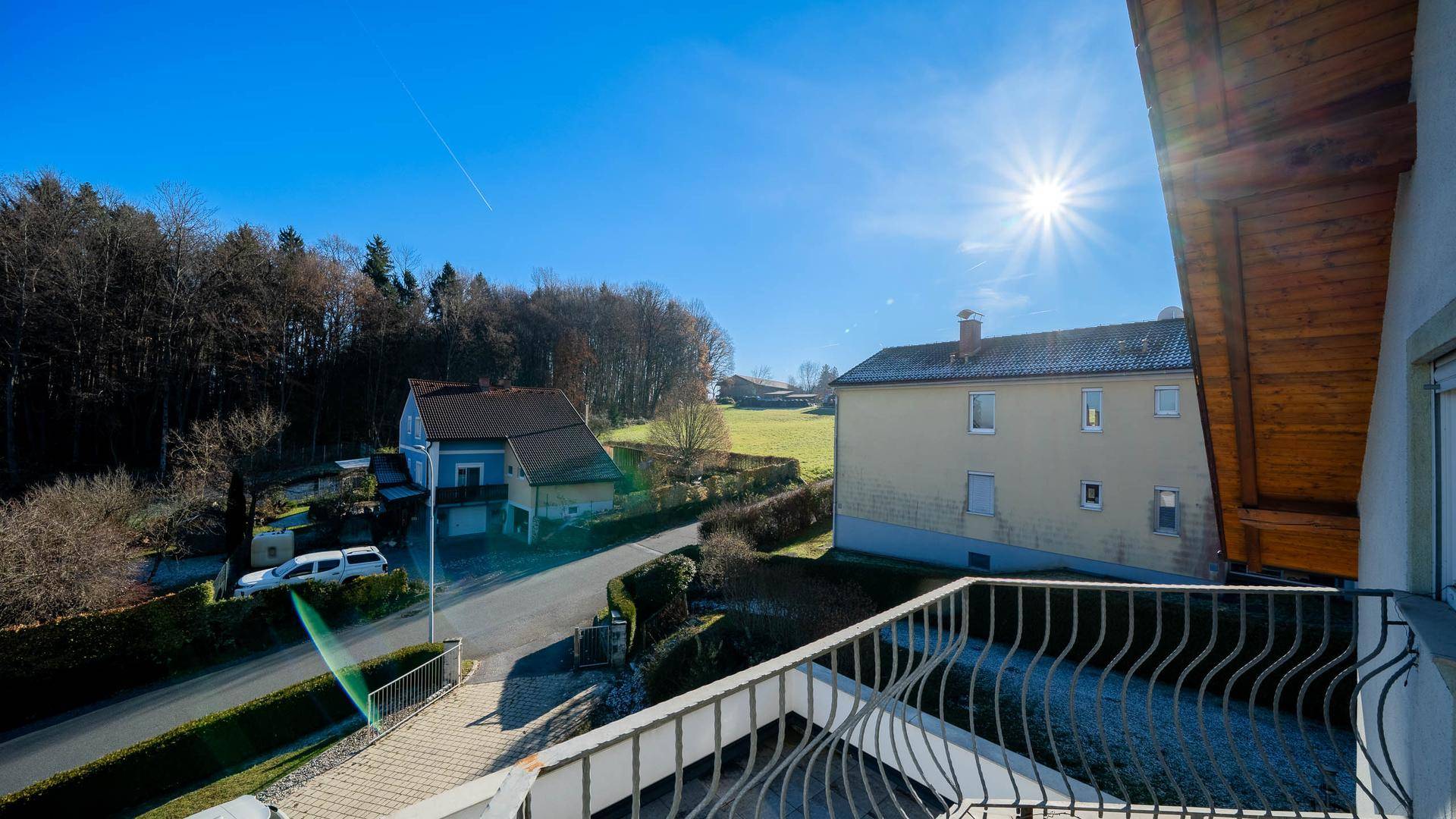 Sonniger Balkon mit weitem Blick über die Landschaft und umliegende Häuser.