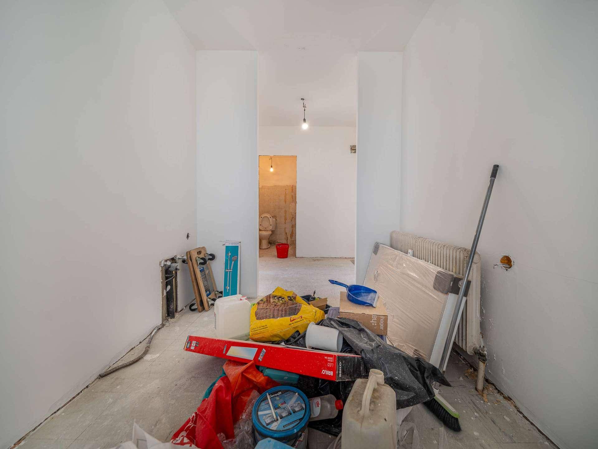 Renovierungsbedürftiger Raum mit Baumaterialien und Blick in einen weiteren Bereich der Wohnung.