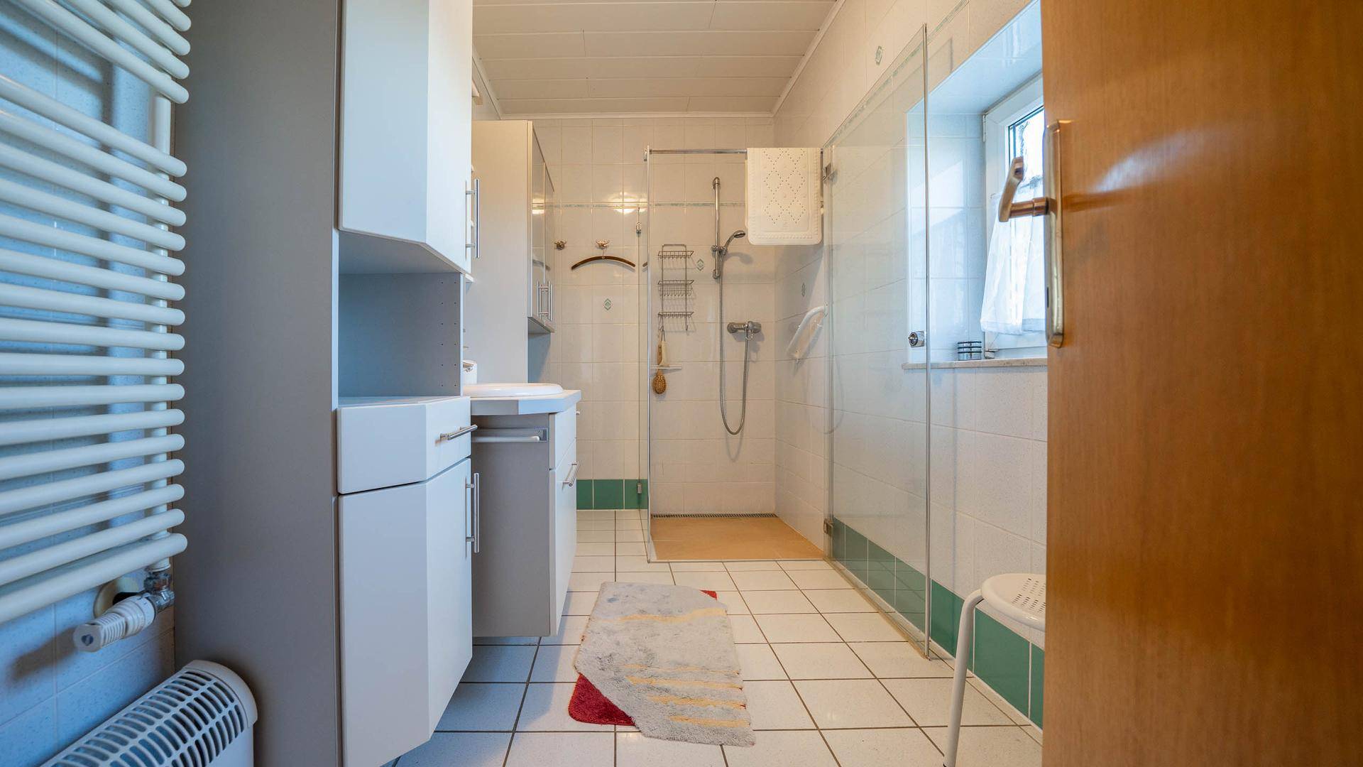 Badezimmer mit Dusche, Waschbecken und beheiztem Handtuchhalter.