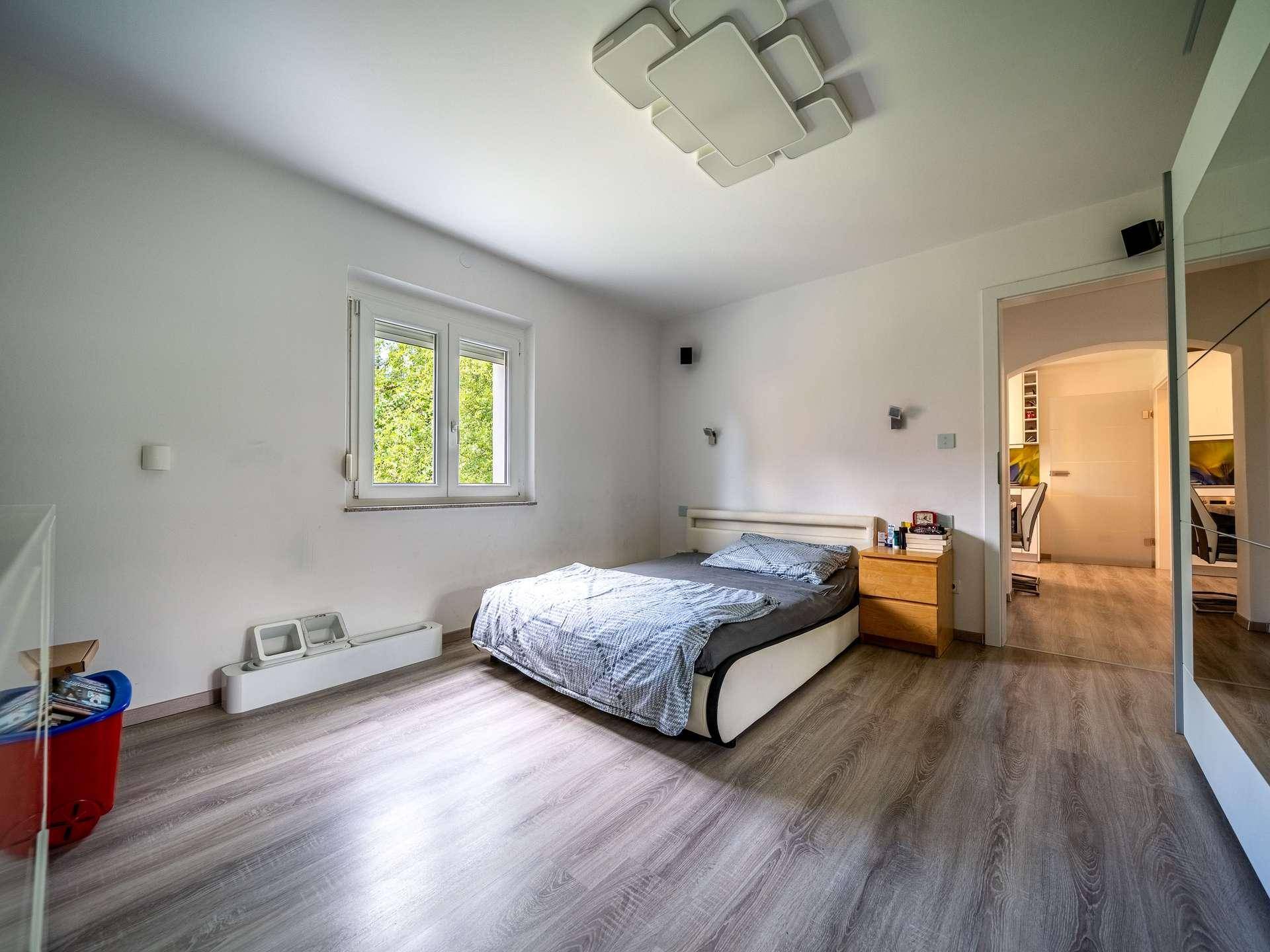 Helles Schlafzimmer mit Bett, Nachttisch und Blick in den Flur.