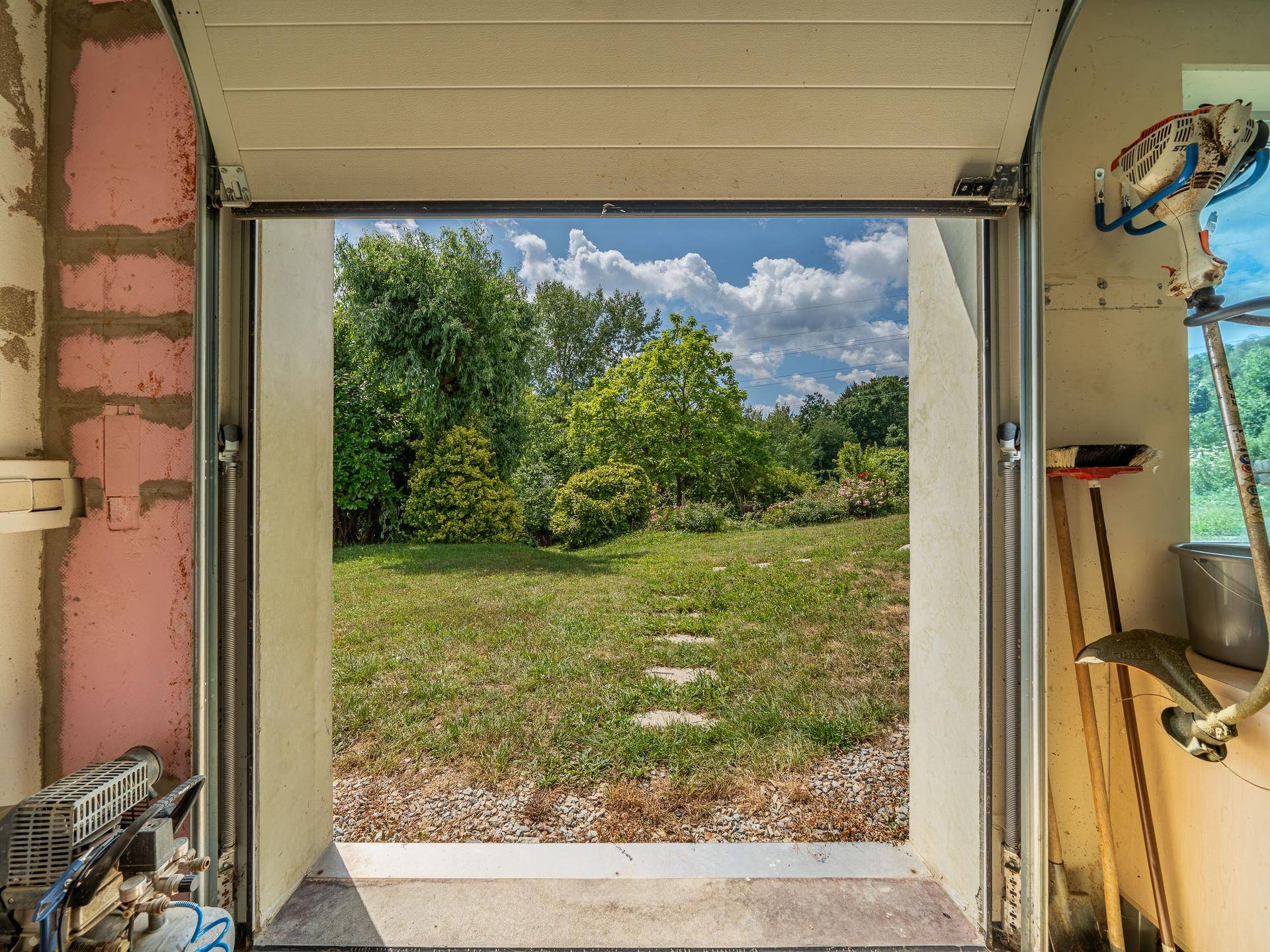 Blick aus der Garage in den gepflegten Garten mit Rasenfläche und Bäumen.