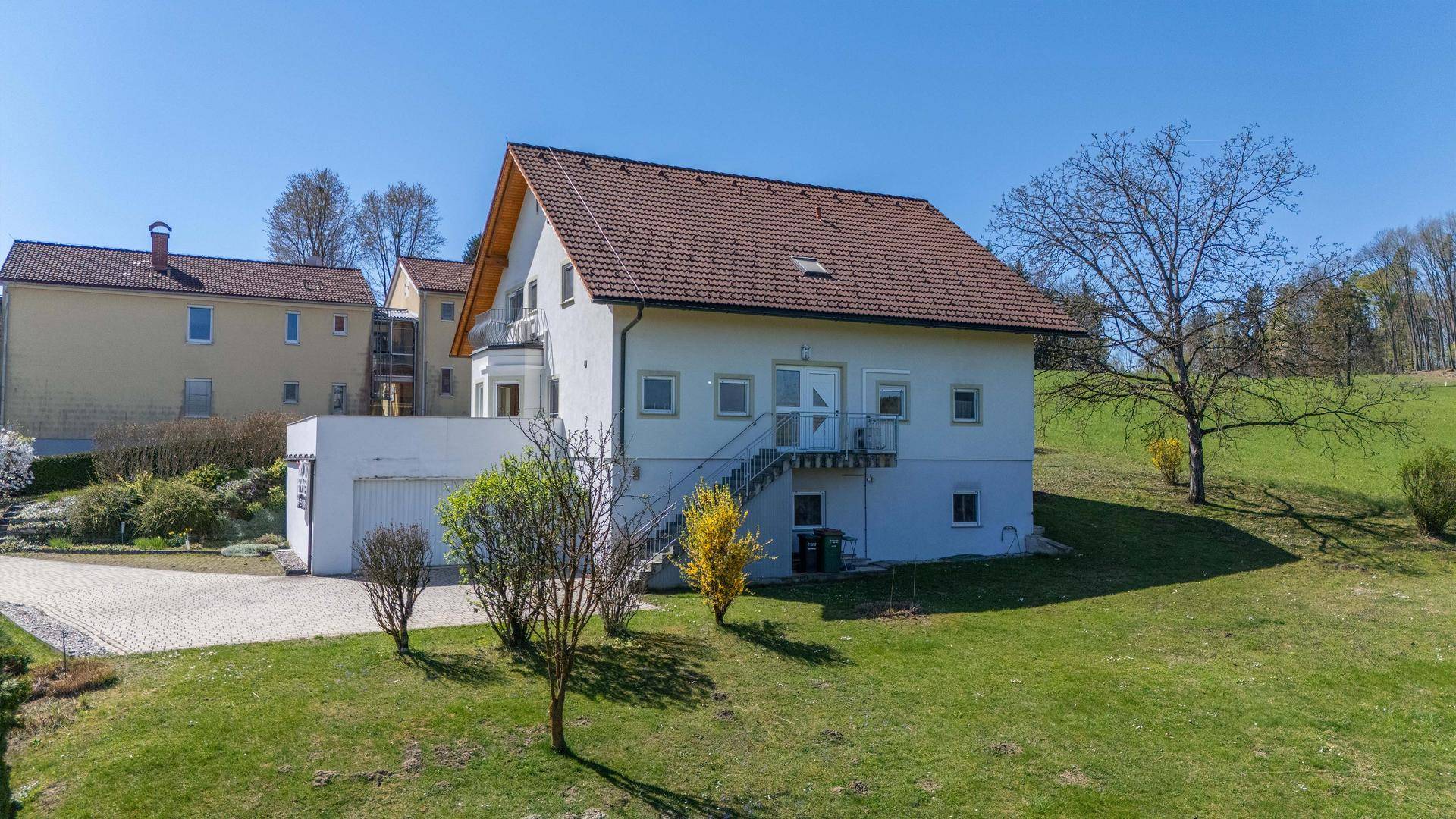 Das Einfamilienhaus mit weißer Fassade und braunem Ziegeldach, eingebettet in eine grüne Umgebung.