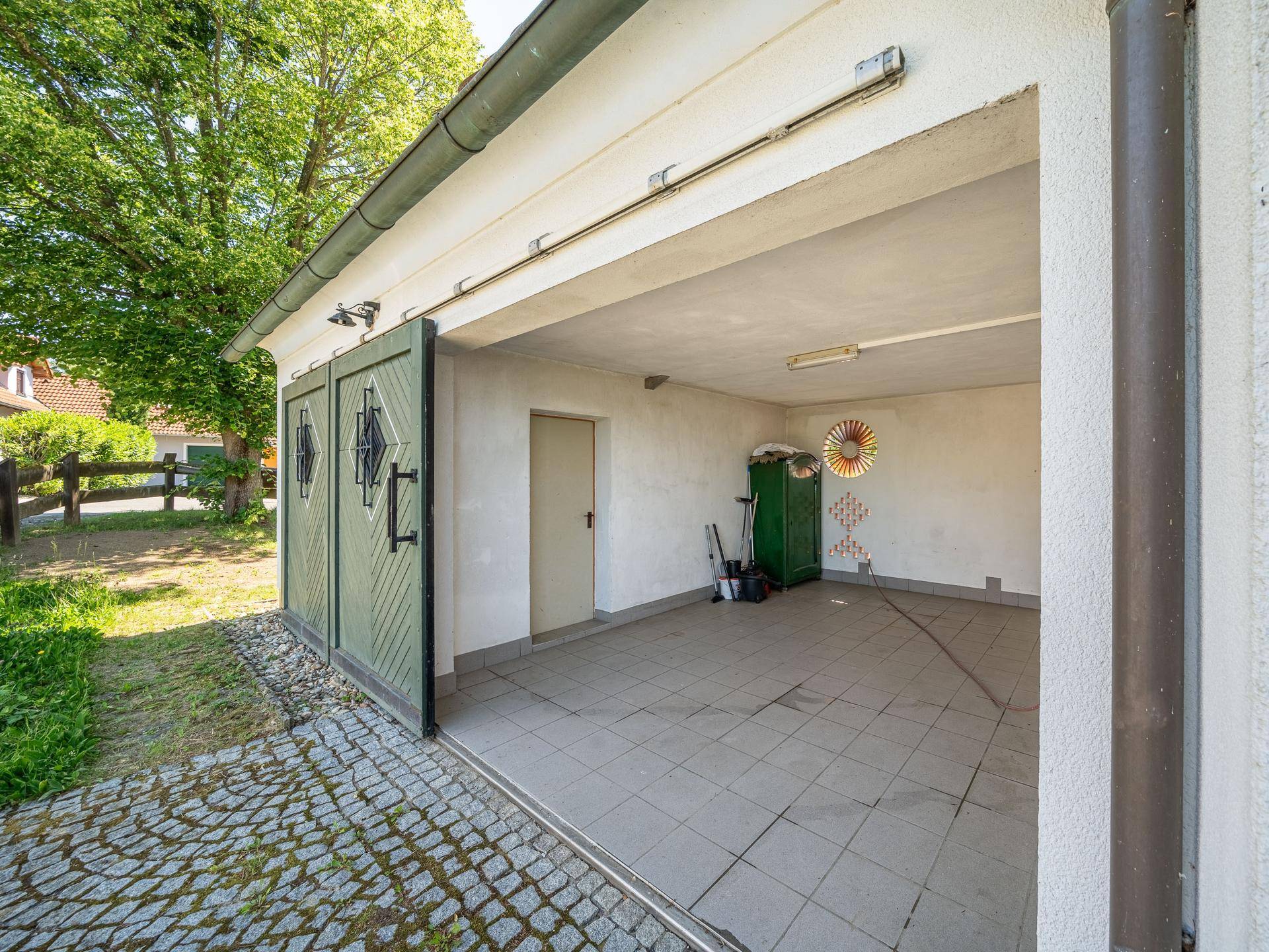 Geräumige Garage mit Fliesenboden und großen grünen Holztüren, offen zur Einfahrt.