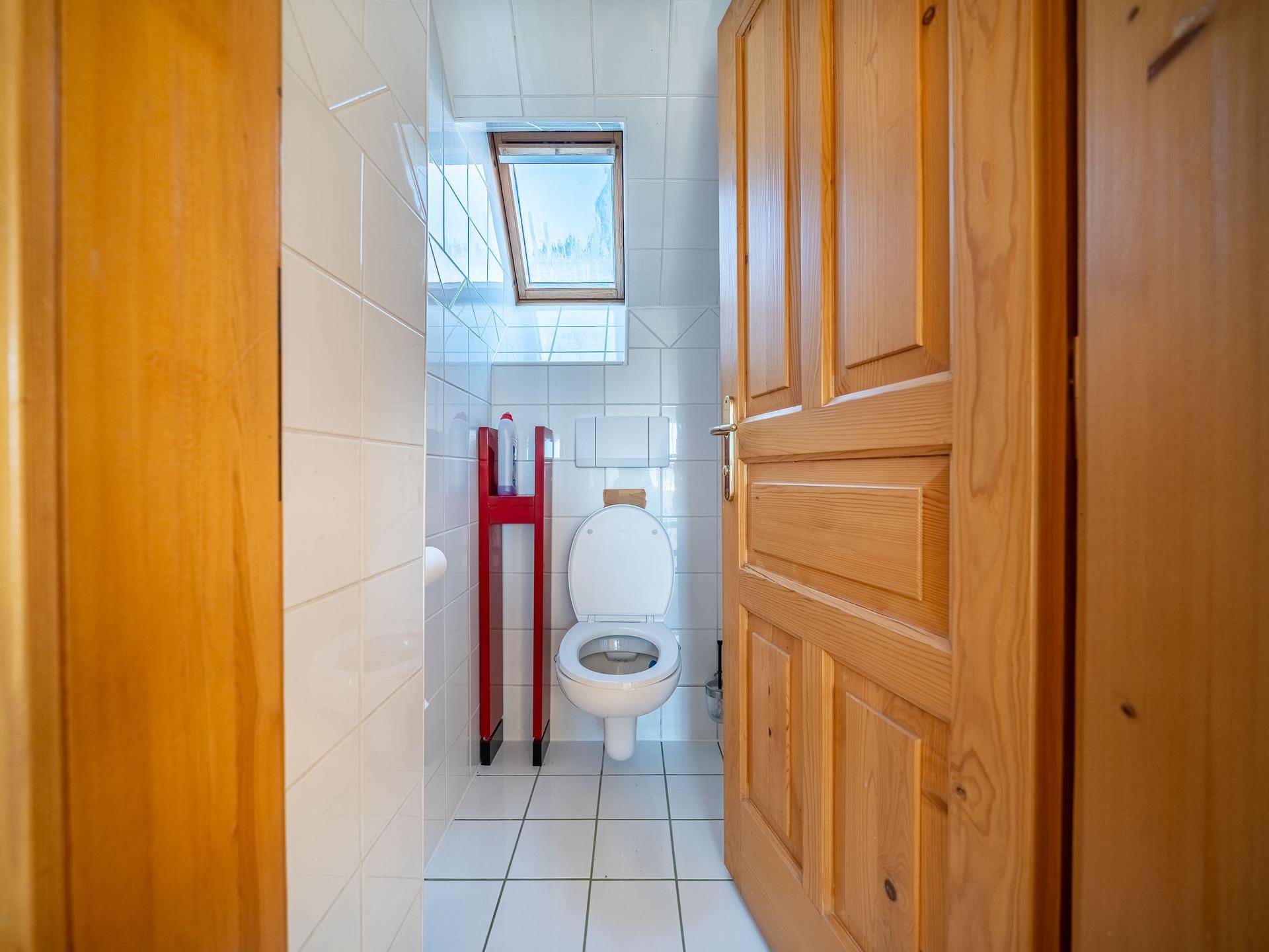 Kleines WC mit weißen Fliesen, Toilette und Dachfenster für natürliches Licht.