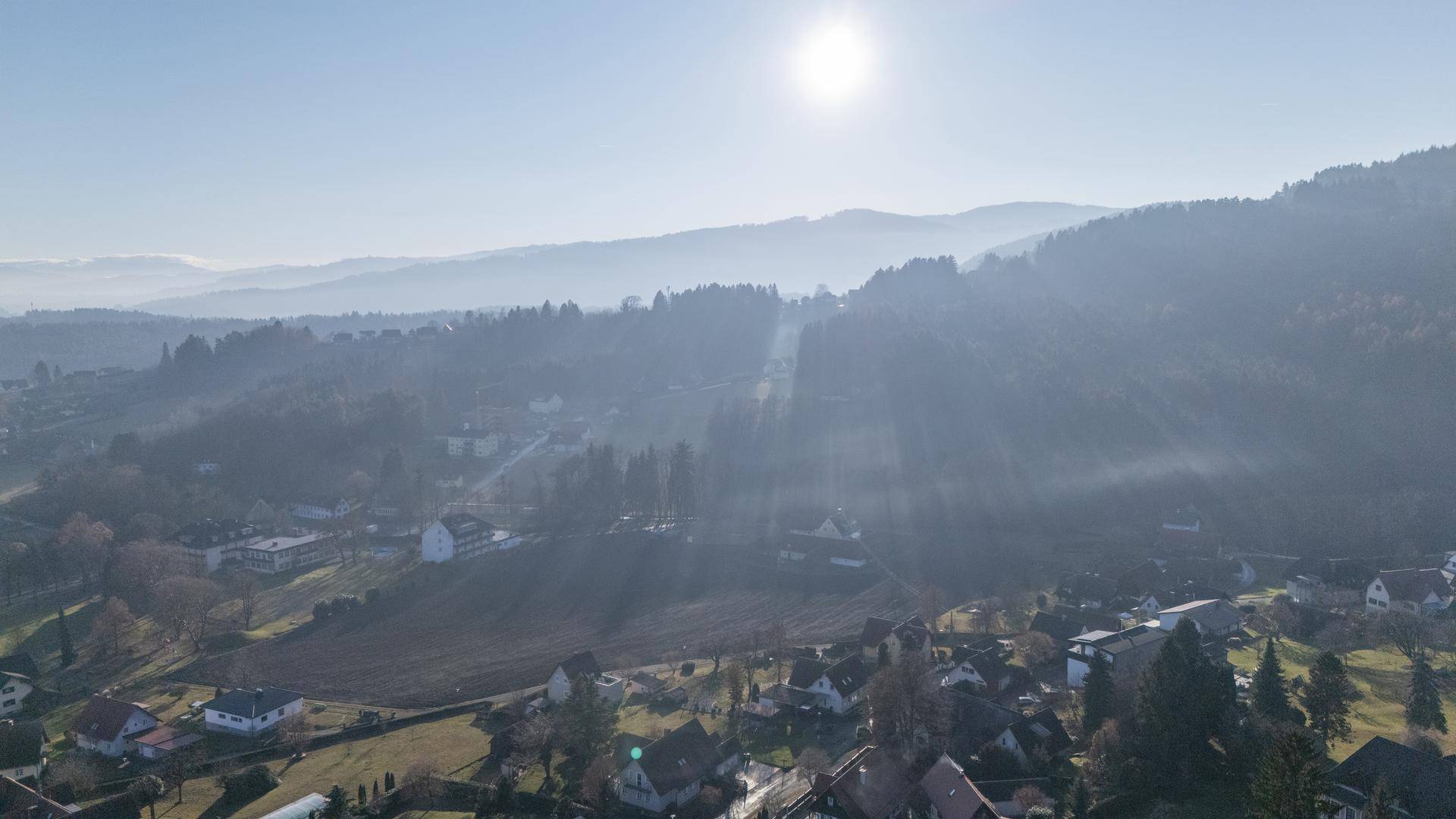 Panoramablick über eine hügelige, bewaldete Landschaft mit verstreuten Häusern und leichter Nebelbildung in den Tälern.