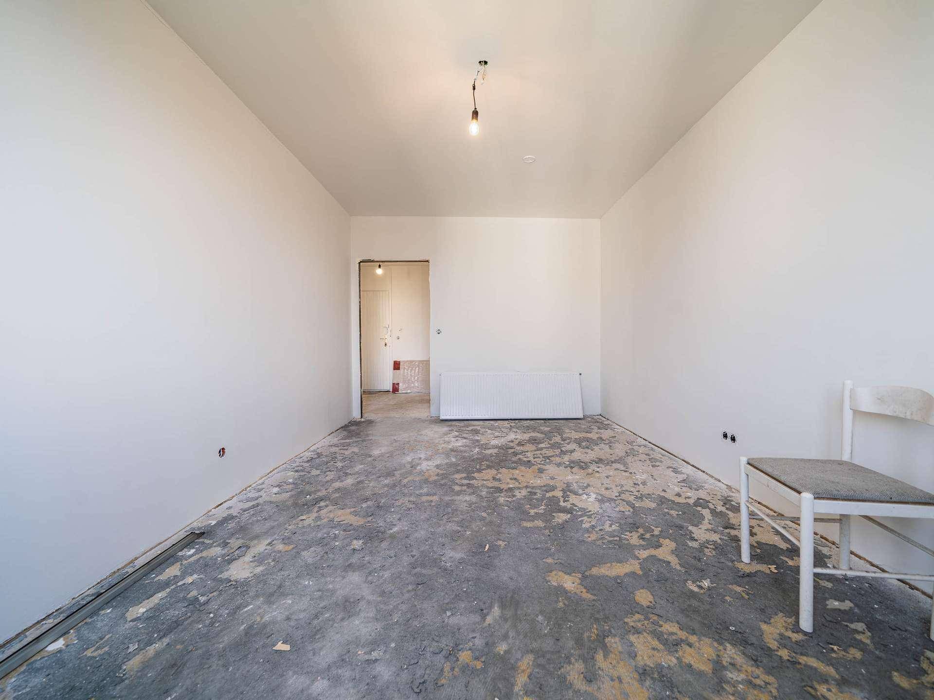 Leeres Zimmer in Renovierung mit Blick auf einen Flur und abgenutztem Bodenbelag.