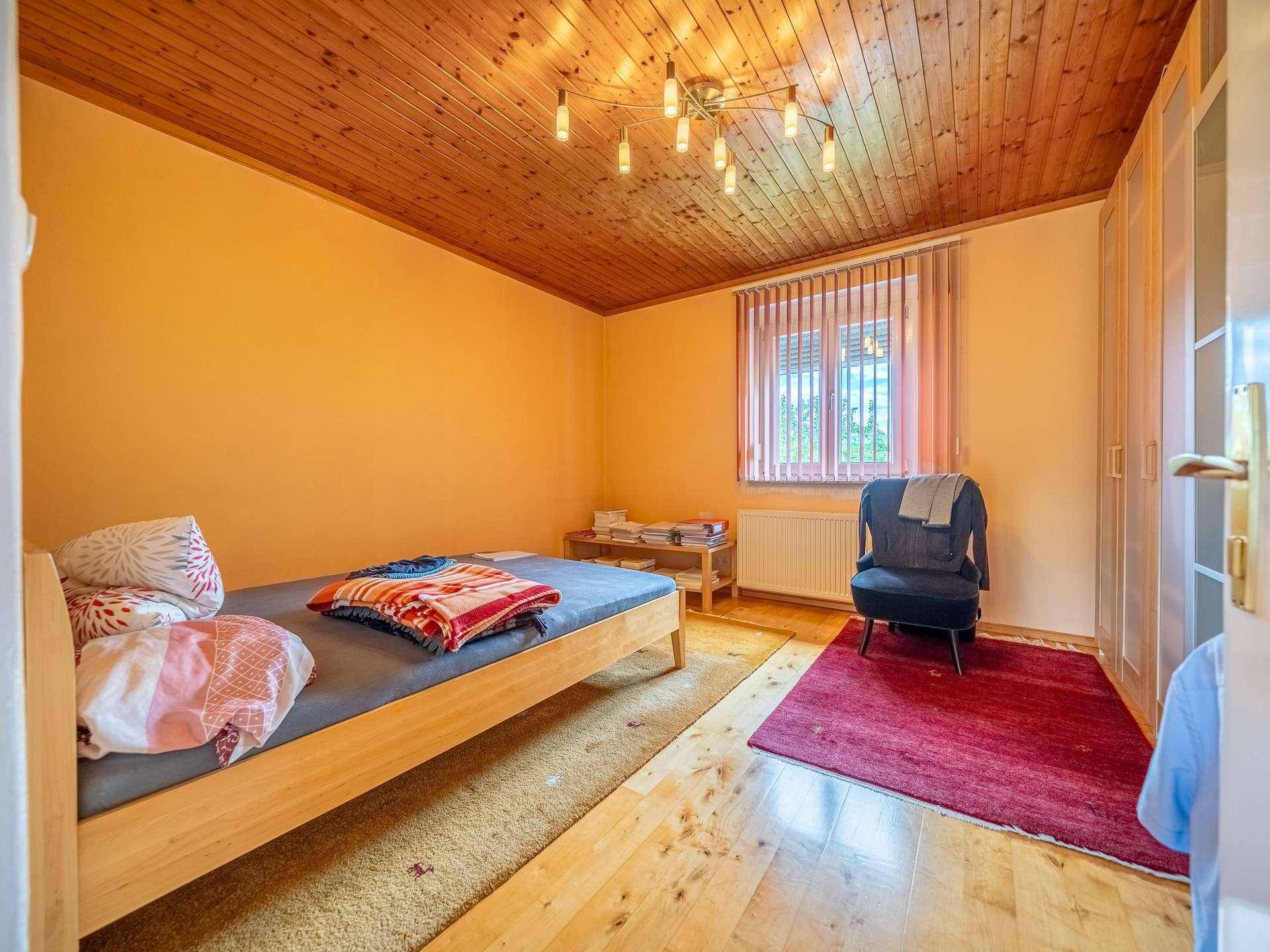 Schlafzimmer mit Holzbalkendecke, Bett und Fenster mit Jalousien.