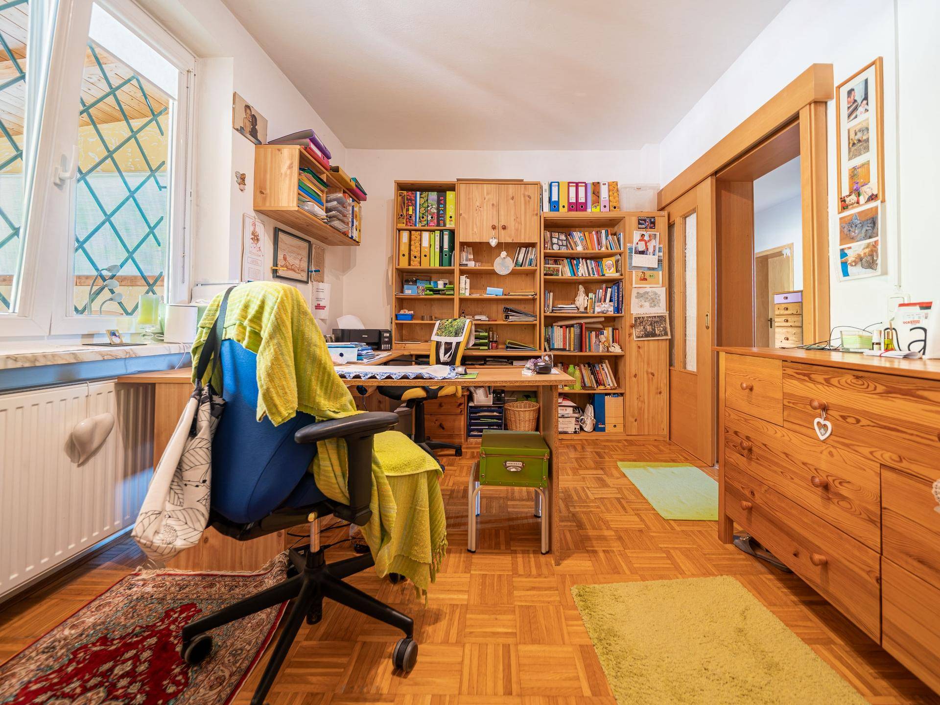 Gemütliches Arbeitszimmer mit Holzmöbeln, Parkettboden und großem Fenster.