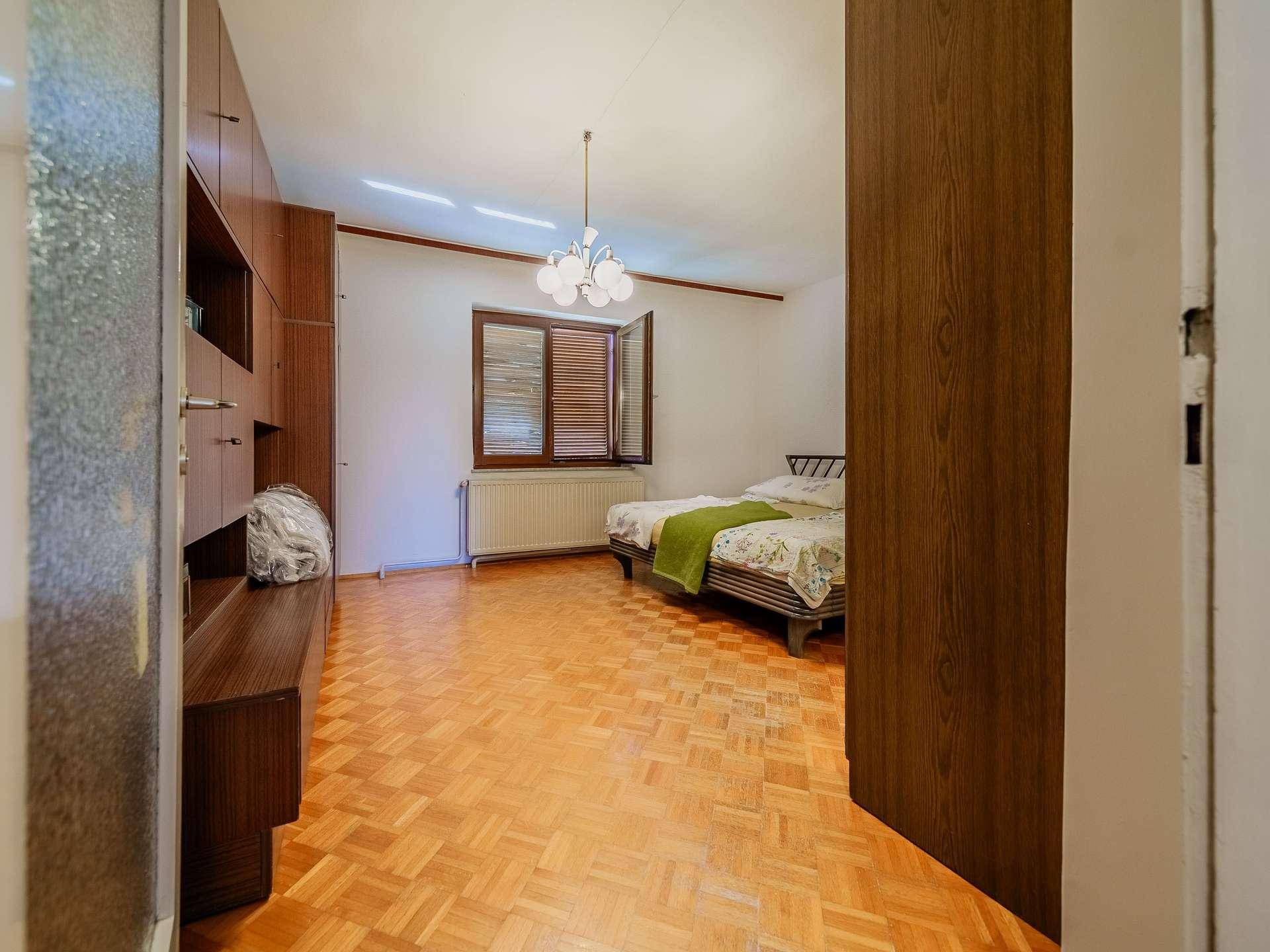 Schlafzimmer mit Parkettboden, Einbauschränken und einem Fenster mit Holzjalousien.