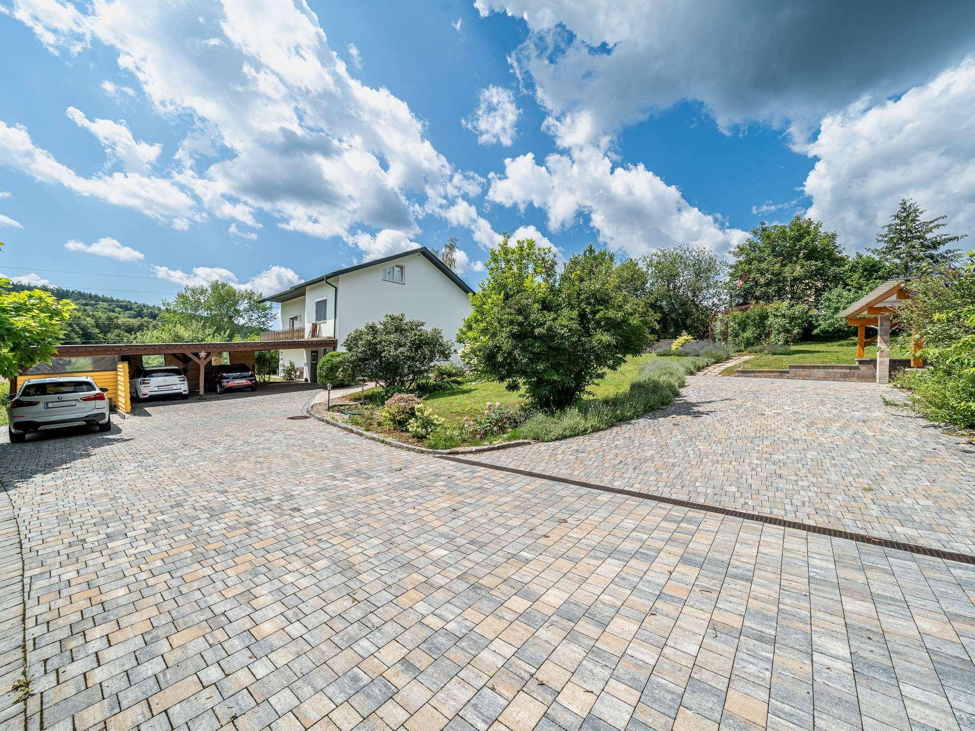 Weitläufige gepflasterte Auffahrt mit Carport und Blick auf das Wohnhaus.