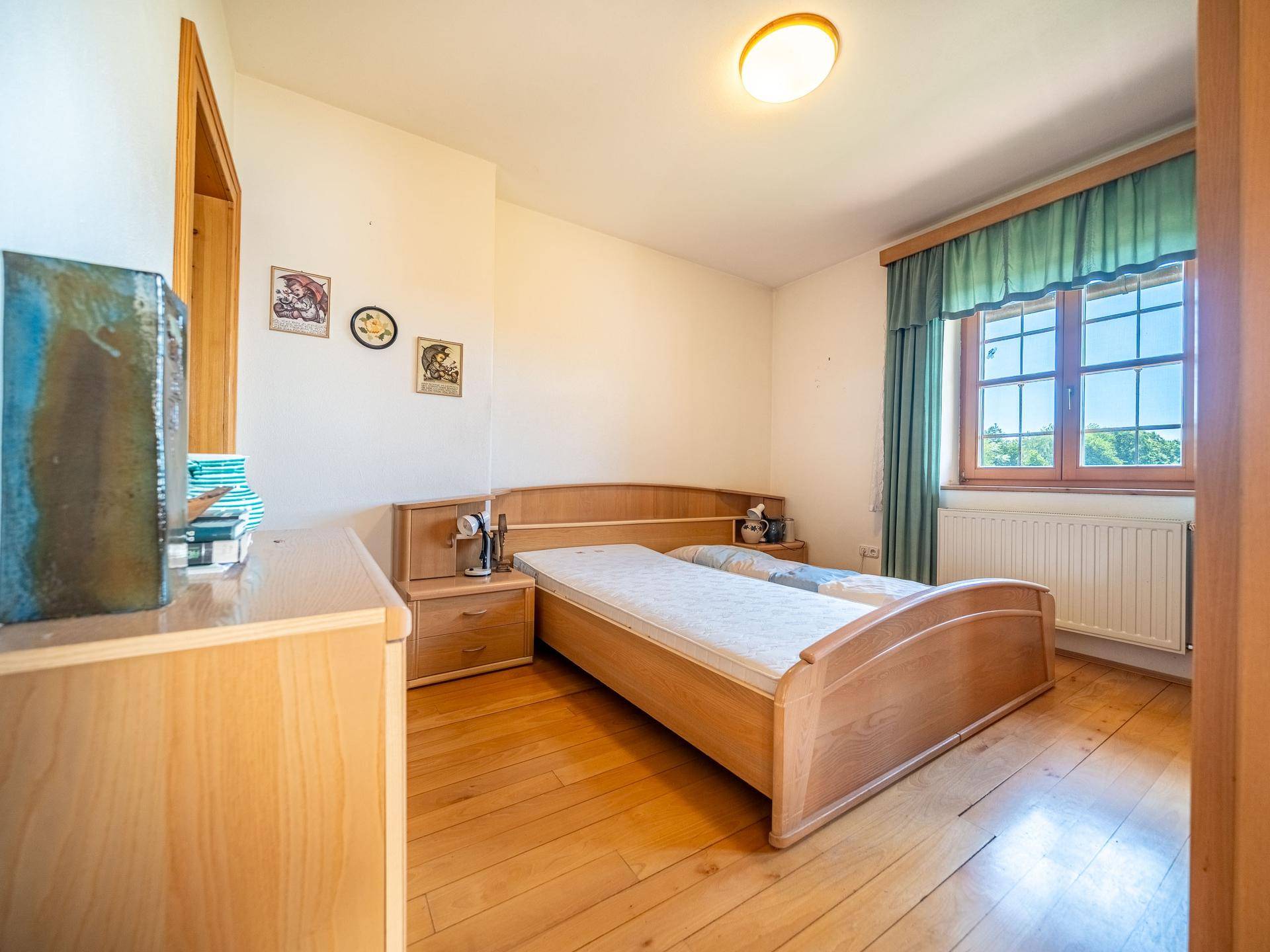 Gemütliches Schlafzimmer mit Holzfußboden, Holzmöbeln und Fenster mit Blick ins Grüne.