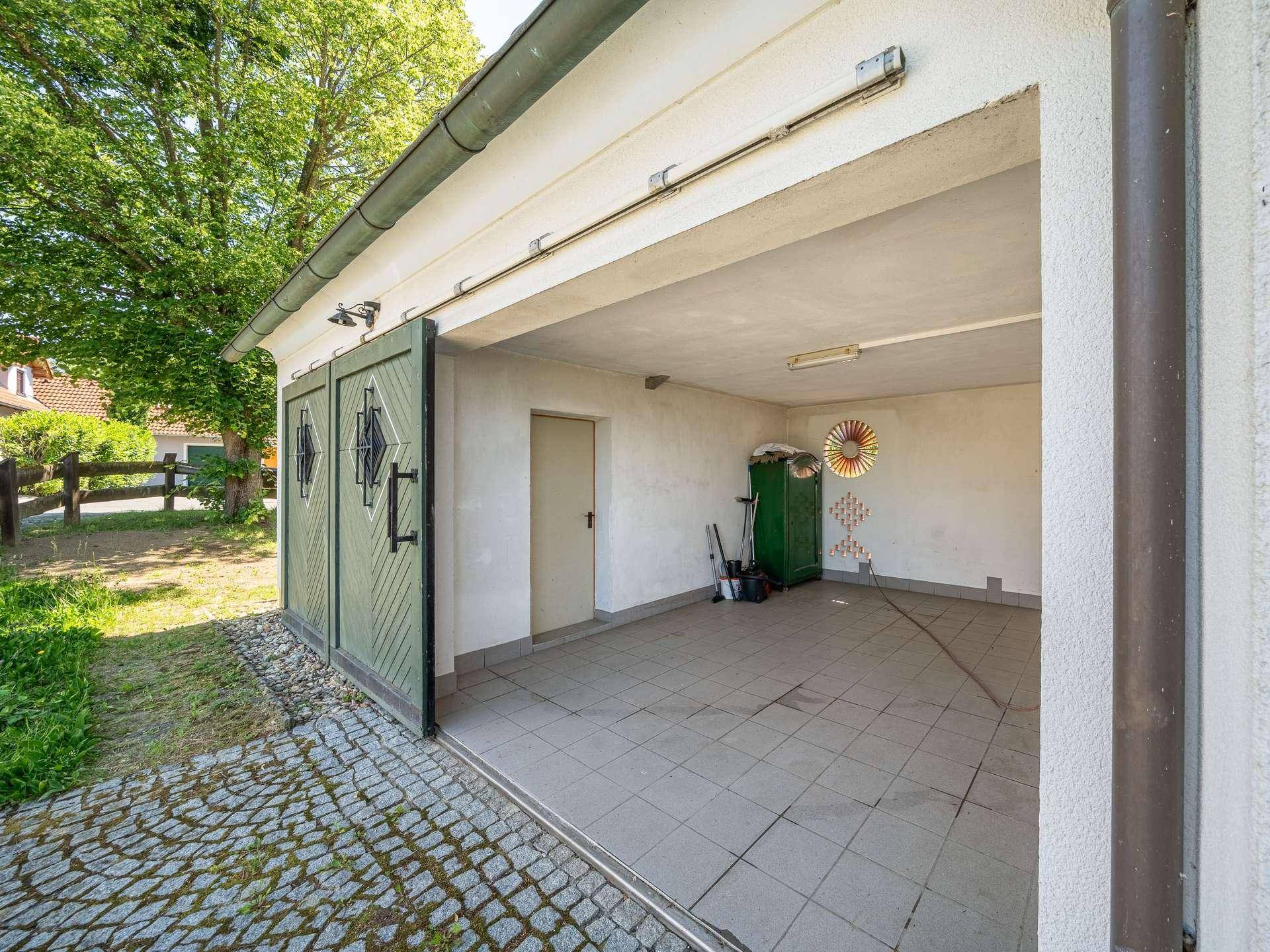 Geräumige Garage mit Fliesenboden und großen Holztoren, ideal für Fahrzeuge und Lagerung.