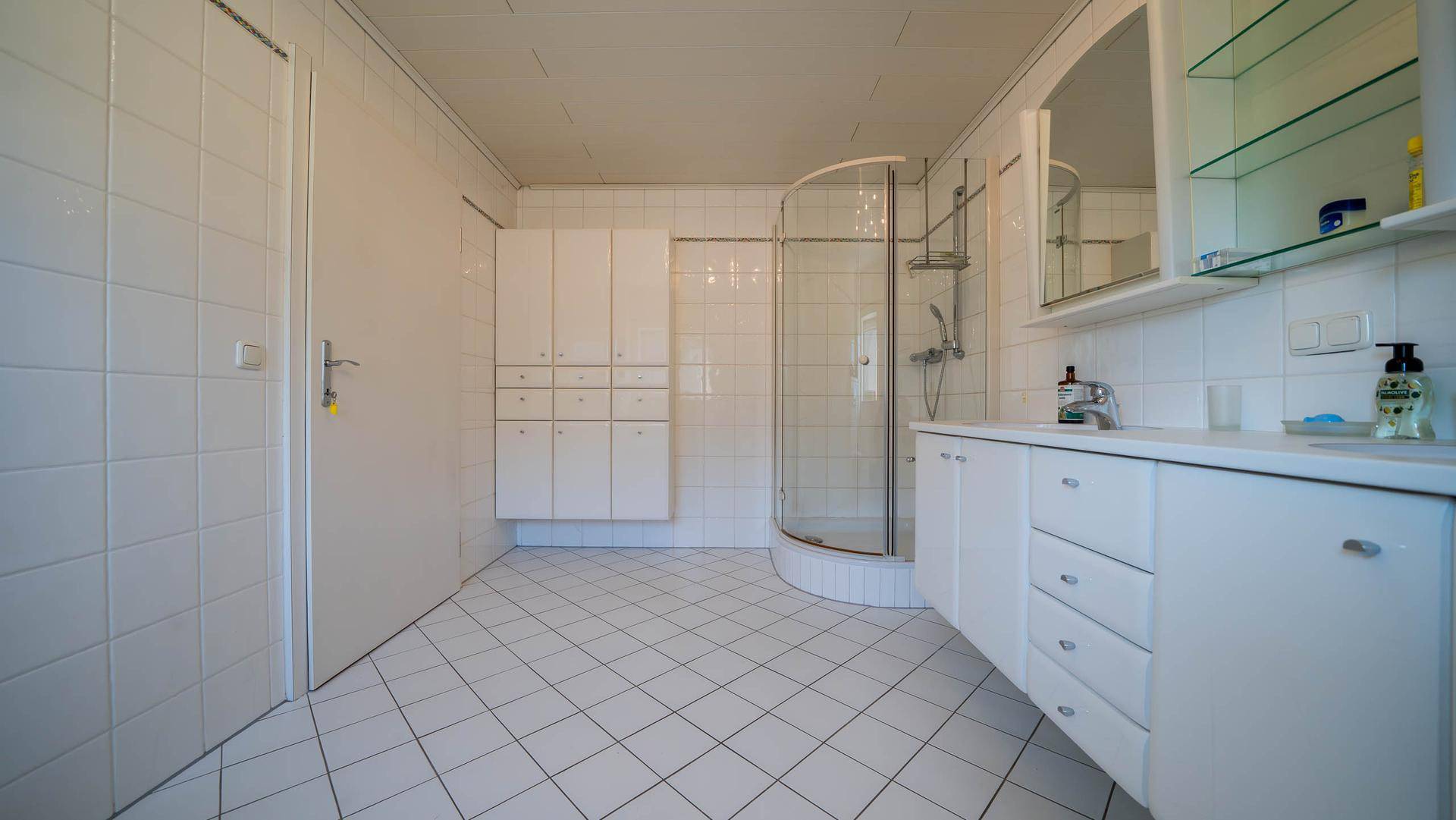 Modern gefliestes Badezimmer mit Dusche, Doppelwaschbecken und weißen Schränken.