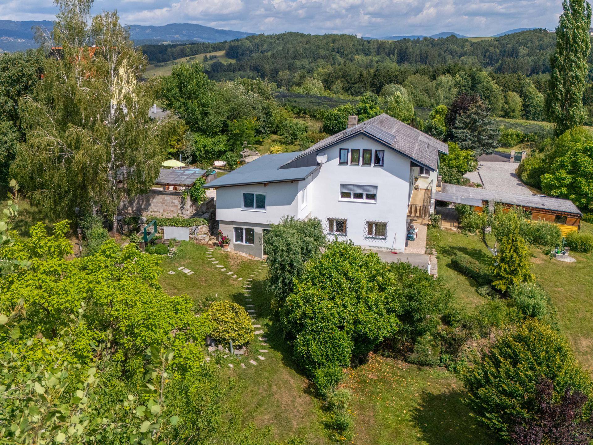 Luftaufnahme des Wohnhauses mit großem Garten, Carport und weitem Blick in die Landschaft.