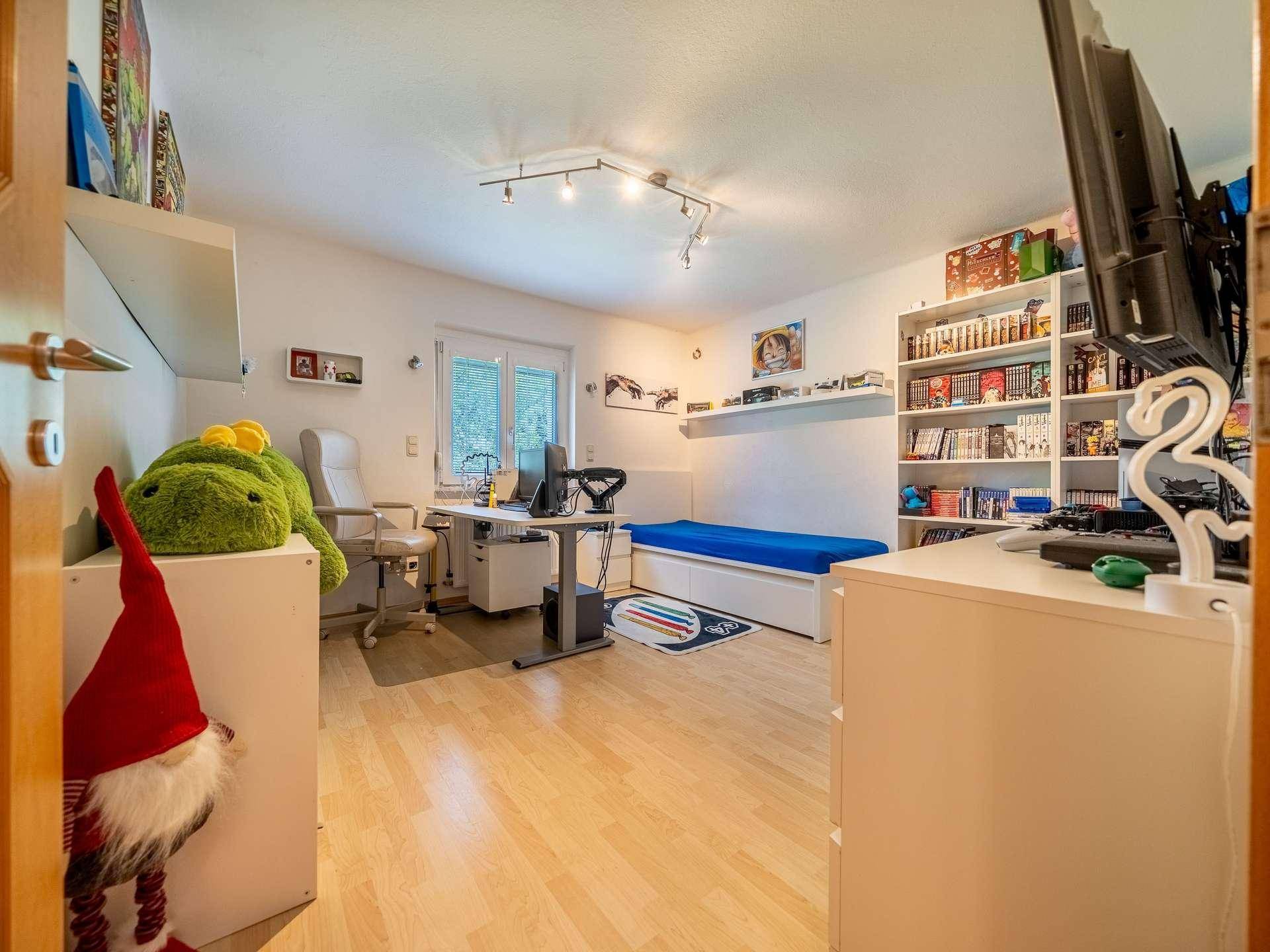 Kinderzimmer oder Büro mit Schreibtisch, Bett und Bücherregal.
