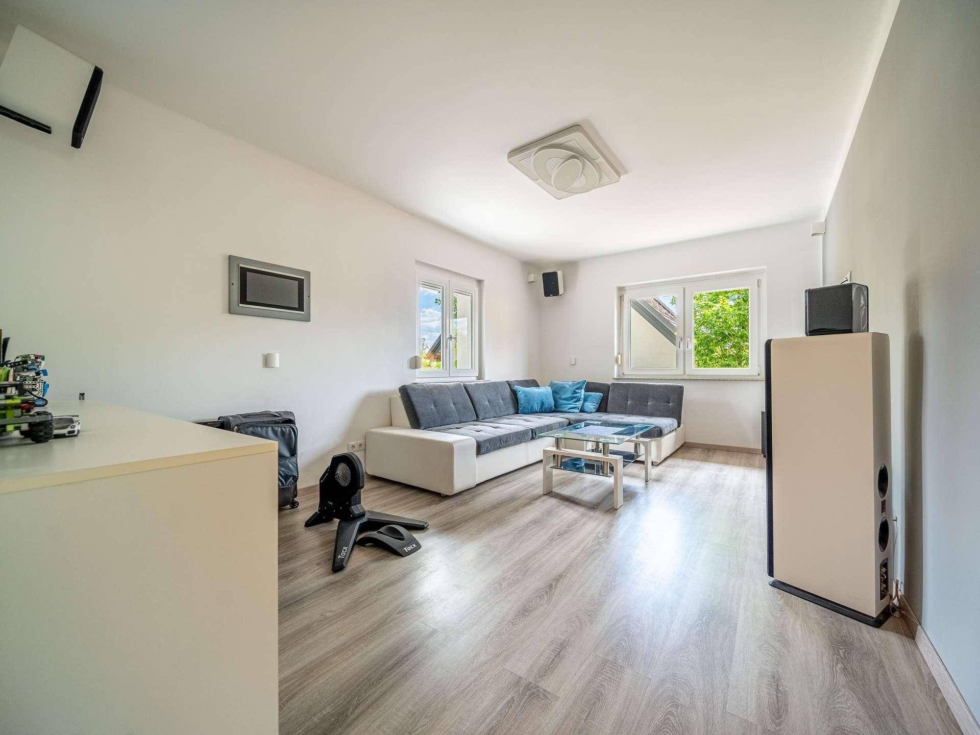 Geräumiges Wohnzimmer mit Ecksofa, Laminatboden und großen Fenstern.