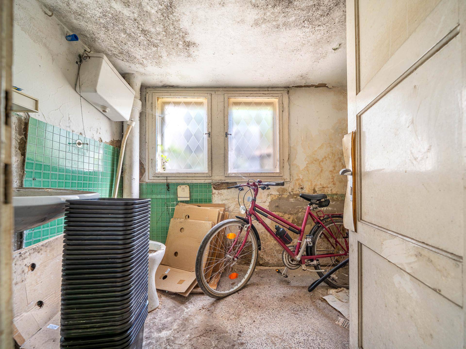 Kellerraum mit Fliesen, Fenster und Fahrrad, der als Waschküche oder Abstellraum dient.