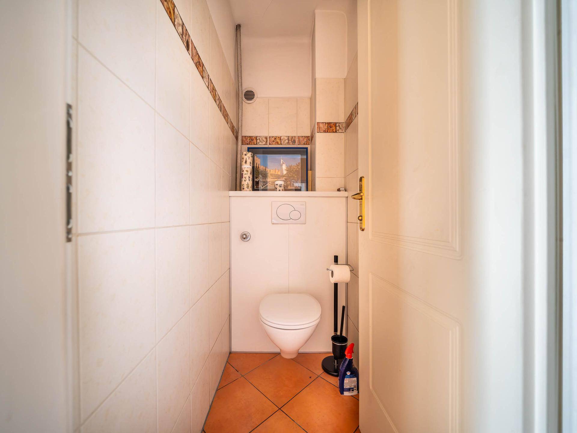 Kleines Gäste-WC mit weißen Fliesen und Terrakotta-Bodenfliesen.
