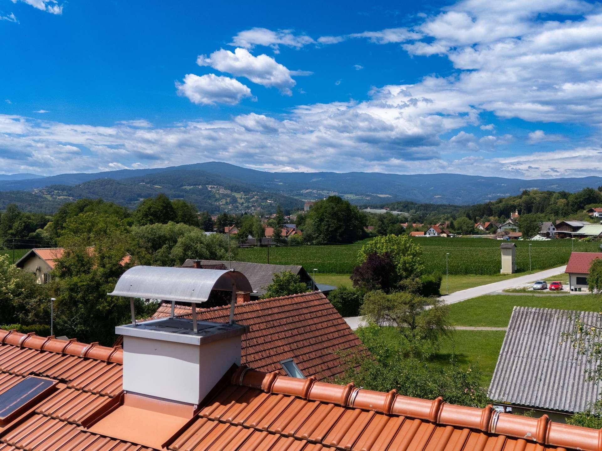 Panoramablick über ländliche Landschaft mit Bergen im Hintergrund und Ziegeldächern.