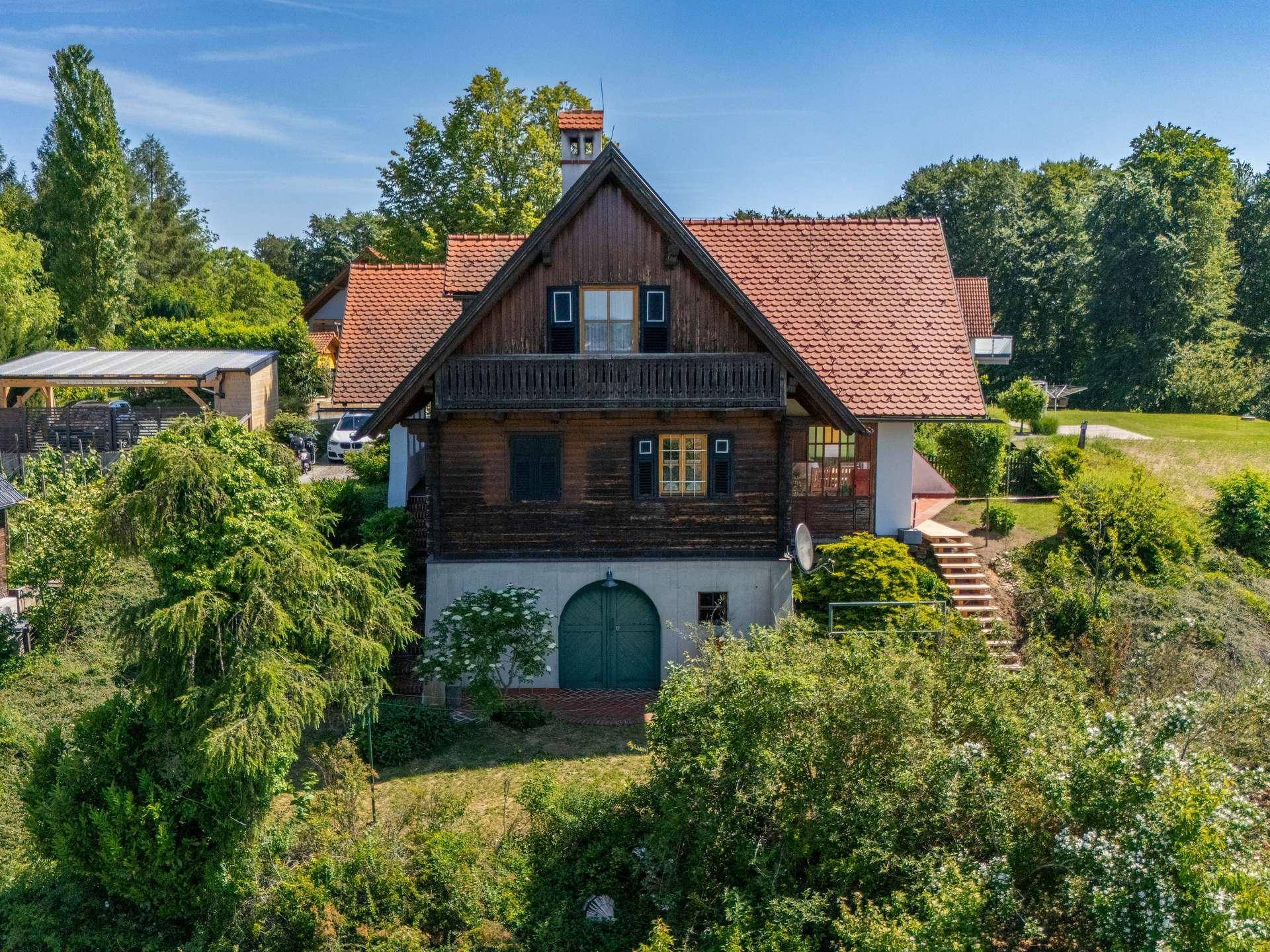 Charmantes Holzhaus mit rotem Ziegeldach, Balkon und grüner Umgebung unter blauem Himmel.