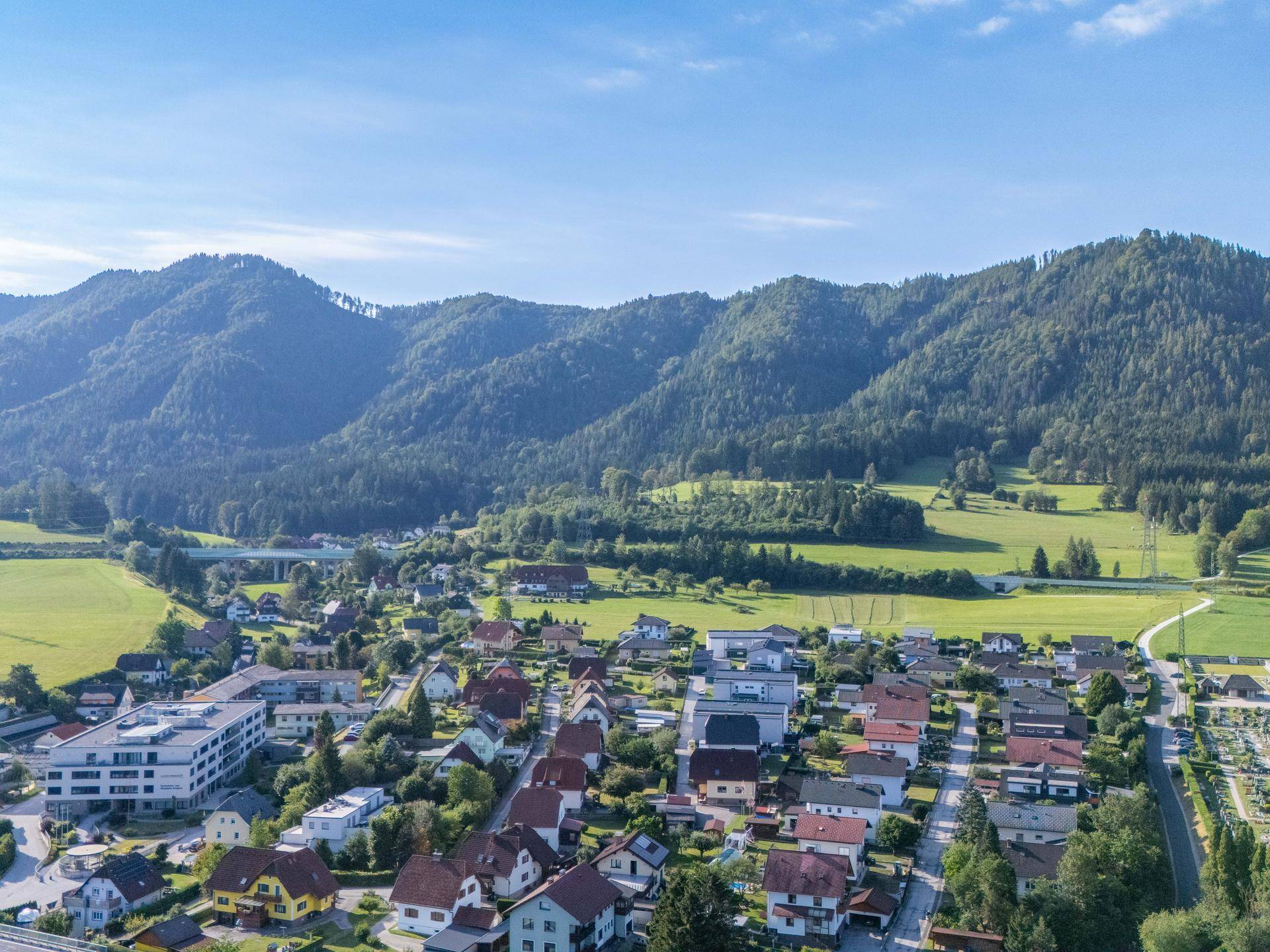 Malerische Ansicht einer Siedlung in einem Tal, umgeben von grünen Wiesen und imposanten Bergen.