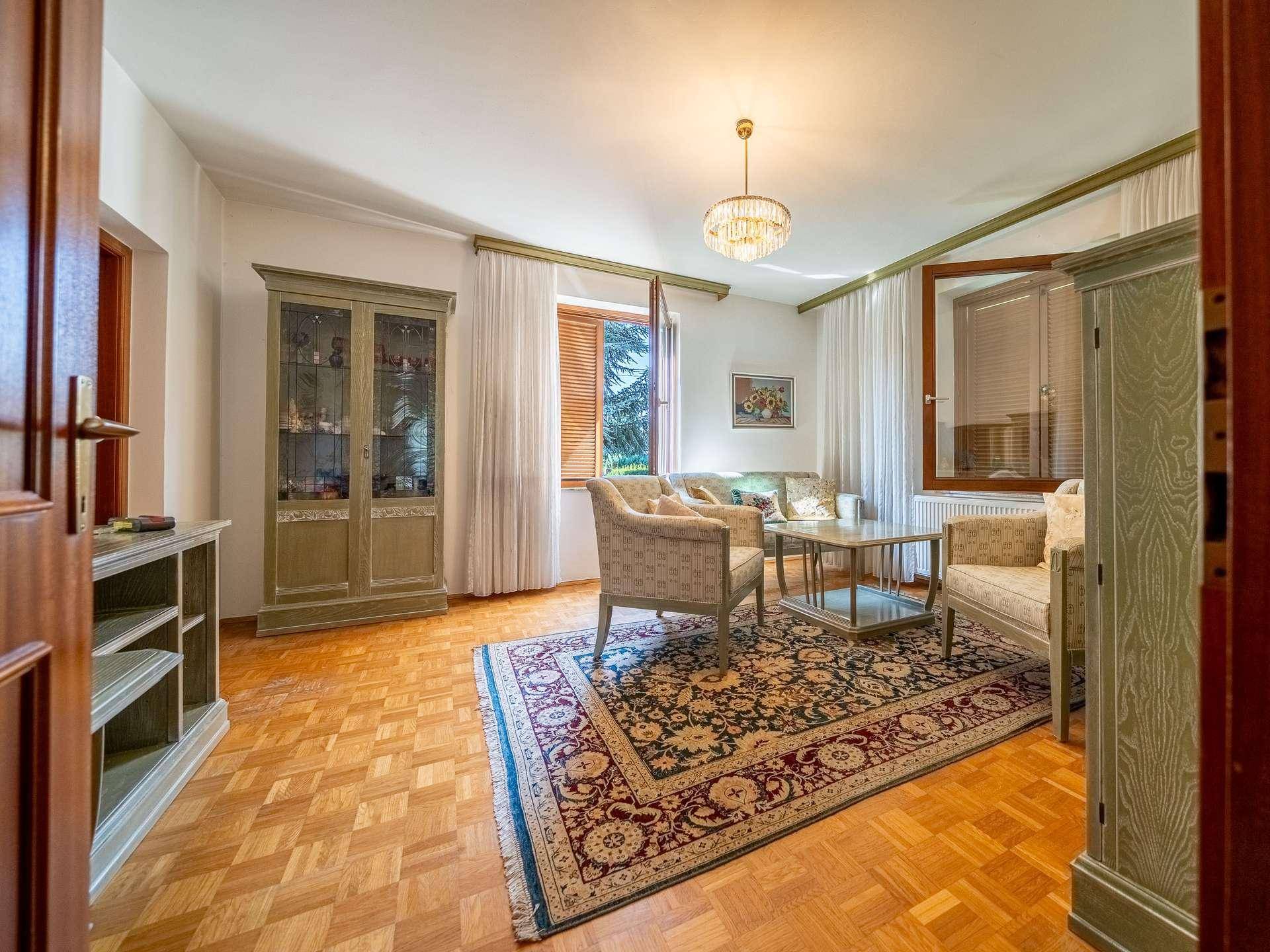 Gemütliches Wohnzimmer mit Parkettboden, Teppich und einem Fenster mit Blick in den Garten.