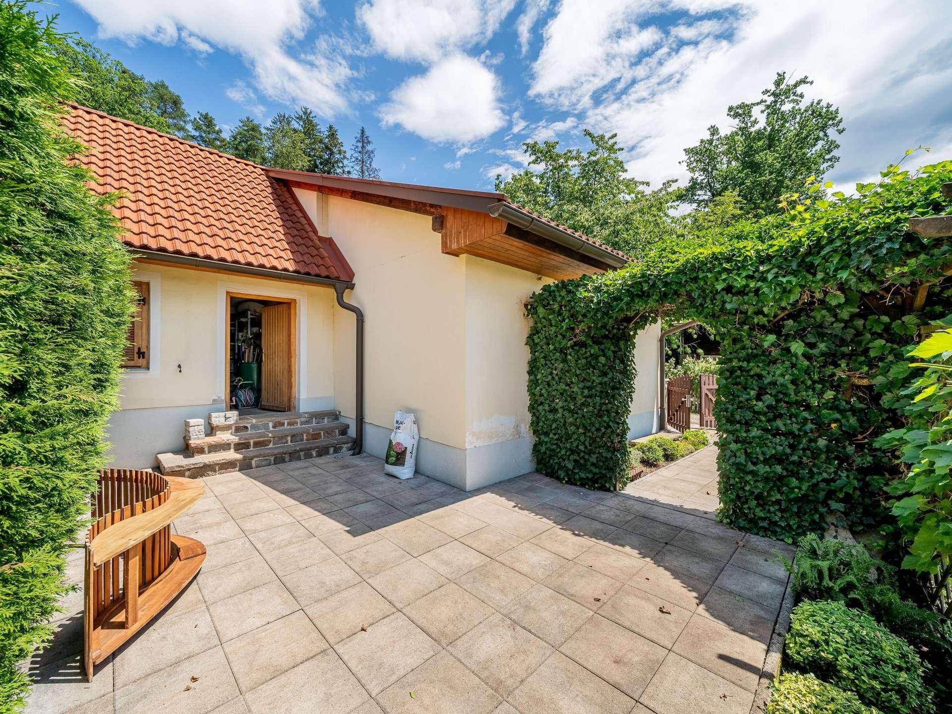 Gepflasterte Terrasse mit Sitzgelegenheit und einem von Efeu bewachsenen Torbogen.