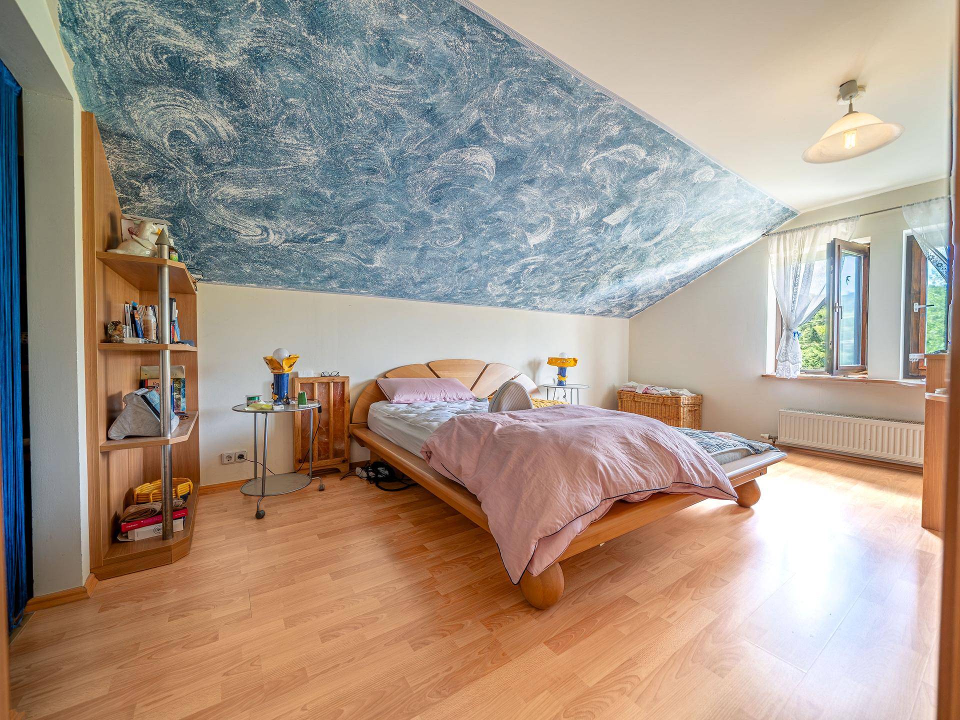 Schlafzimmer im Dachgeschoss mit Laminatboden, blau gemusterter Decke und Fenster.