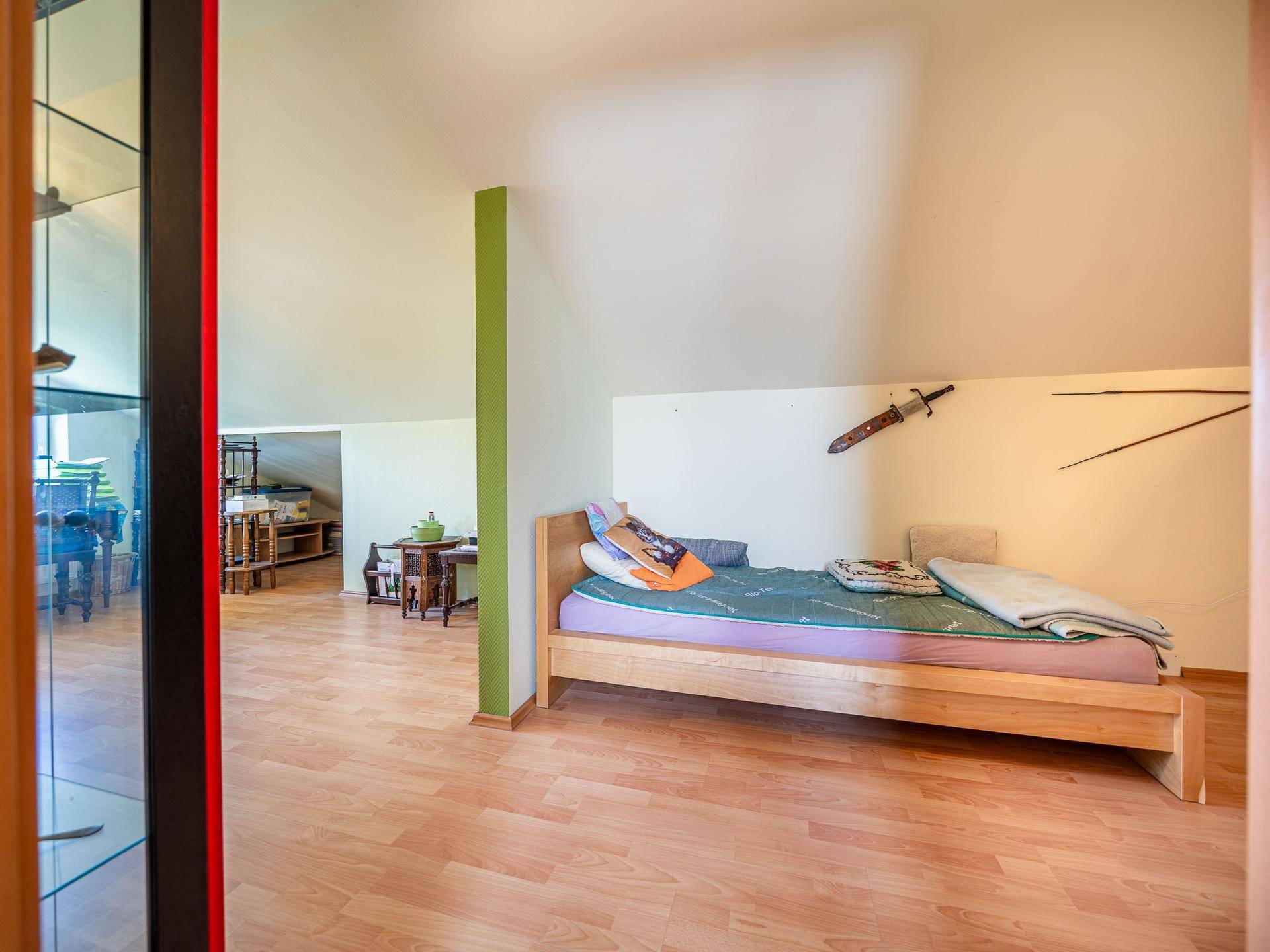 Dachgeschosszimmer mit Holzbett, Laminatboden und Blick in den angrenzenden Bereich.