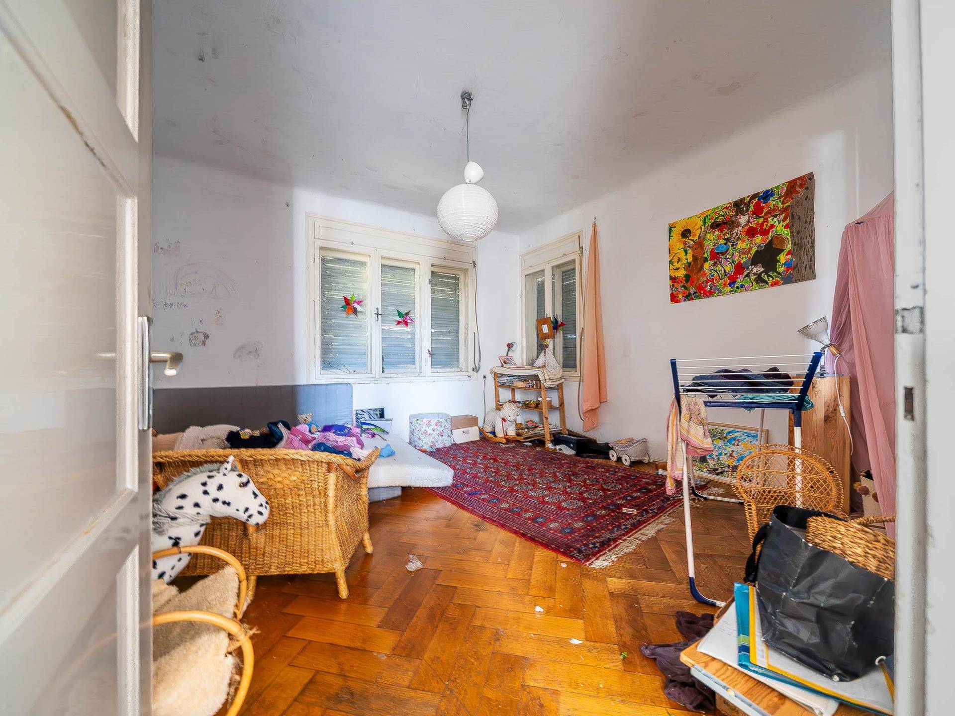 Kinderzimmer mit Parkettboden, Fenster und Spielzeug, das Renovierung benötigt.