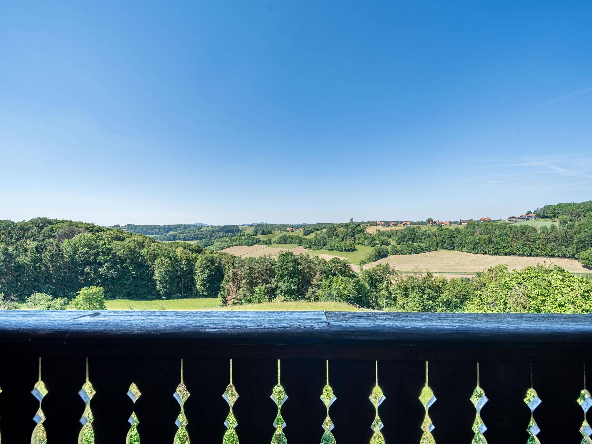Malerischer Ausblick vom Balkon auf sanfte Hügel, Wälder und Felder unter blauem Himmel.