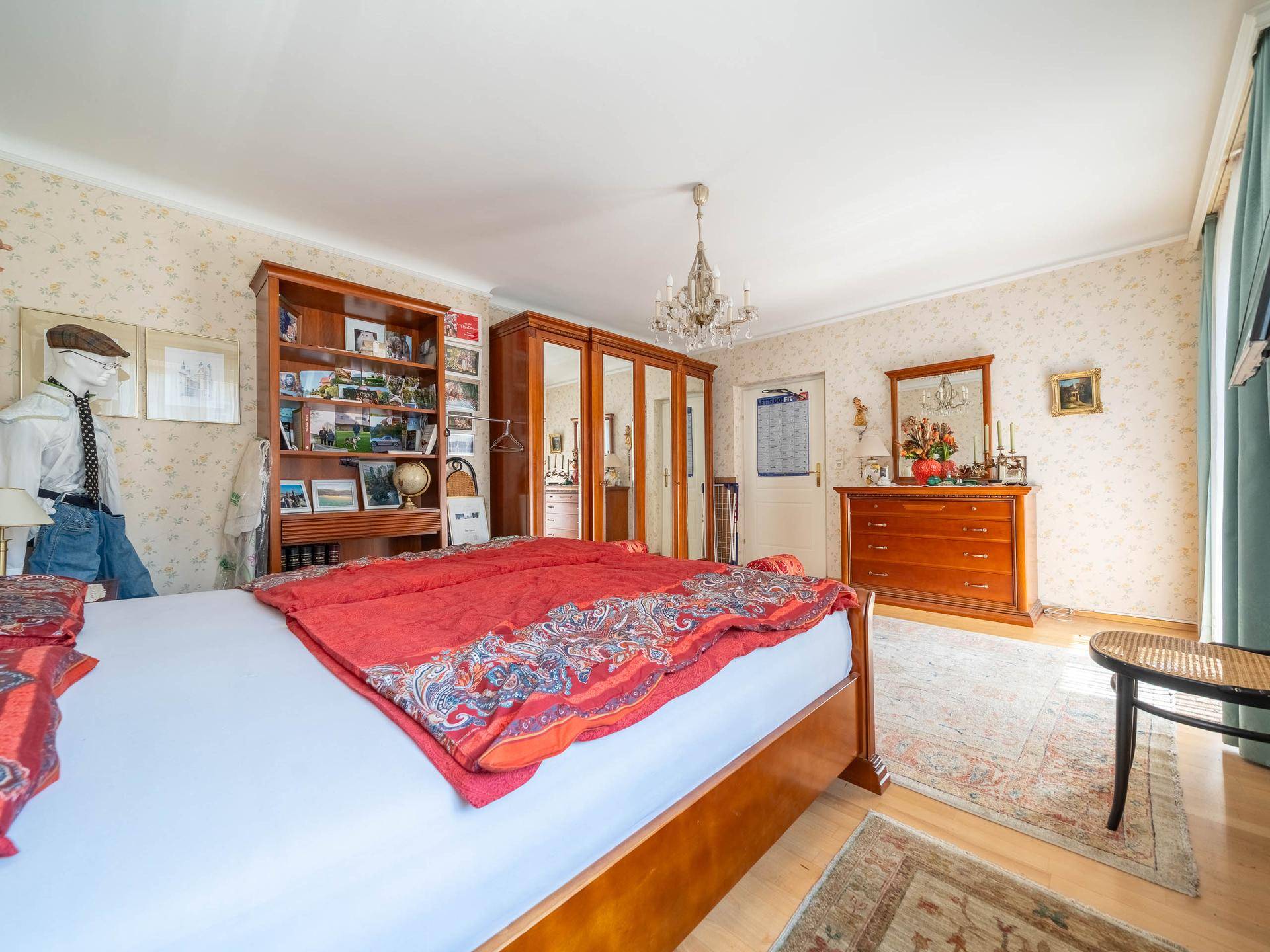 Schlafzimmer mit großem Bett, Holzmöbeln und gemusterter Tapete.