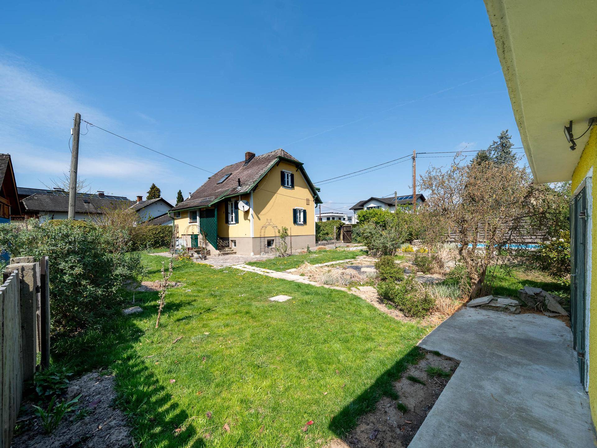 Gelbes Einfamilienhaus mit grünen Fensterläden und großem Garten unter blauem Himmel.