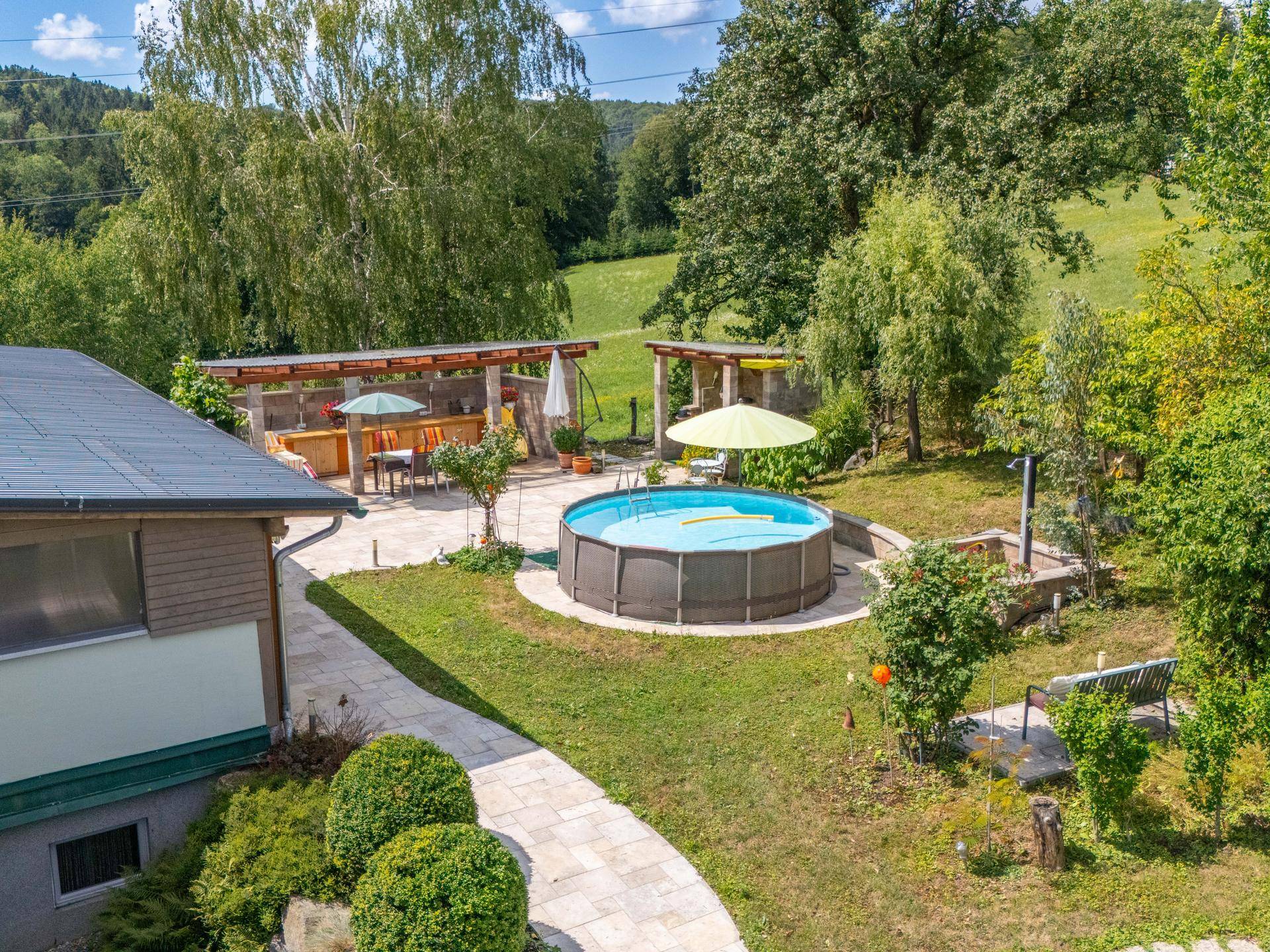 Luftaufnahme des Anwesens mit einem Aufstellpool, großer Terrasse und umgebendem Grün.